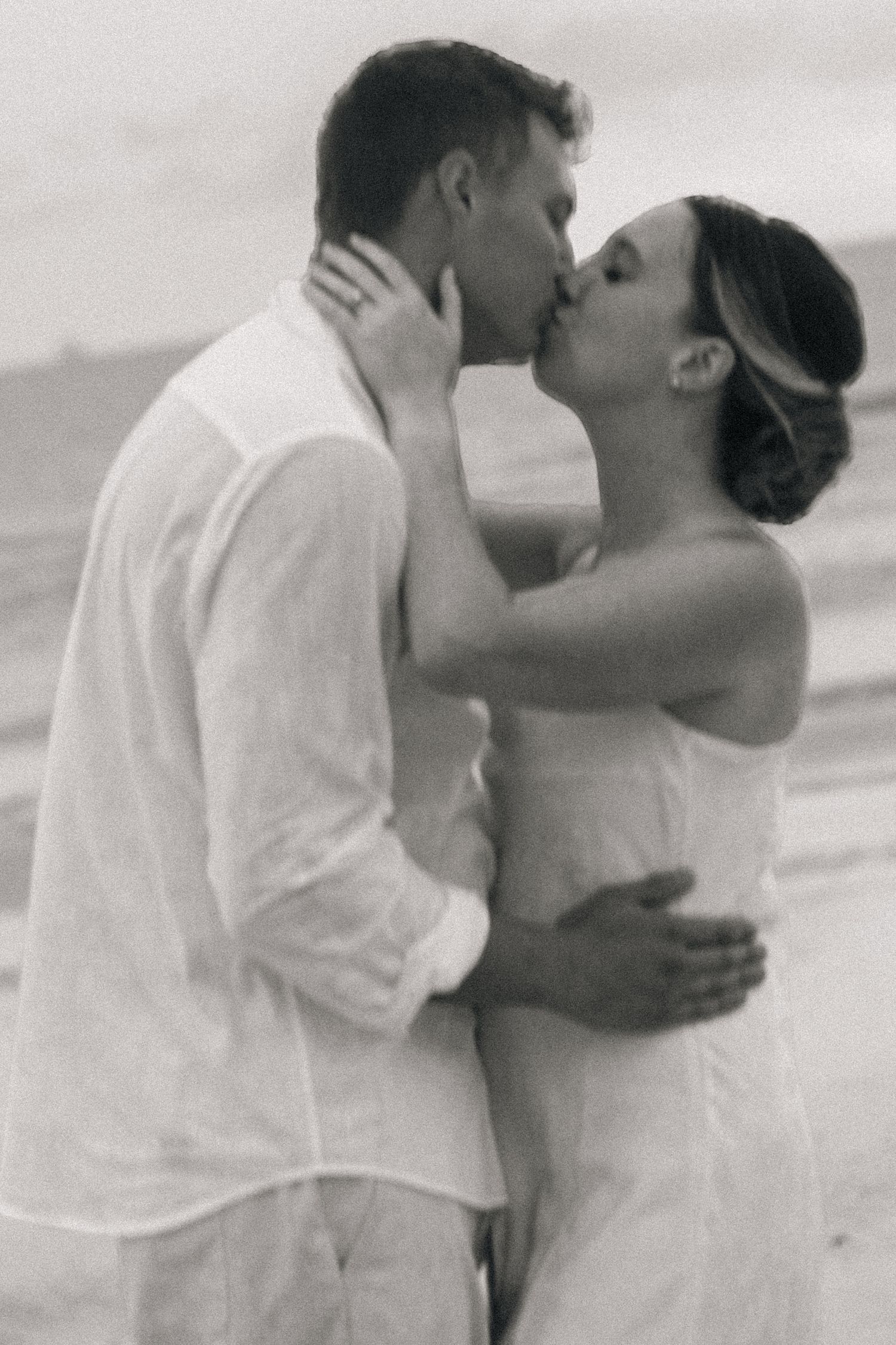 Black and white close-up of a couple kissing on the beach, the bride's hand gently resting on her husband's face.
