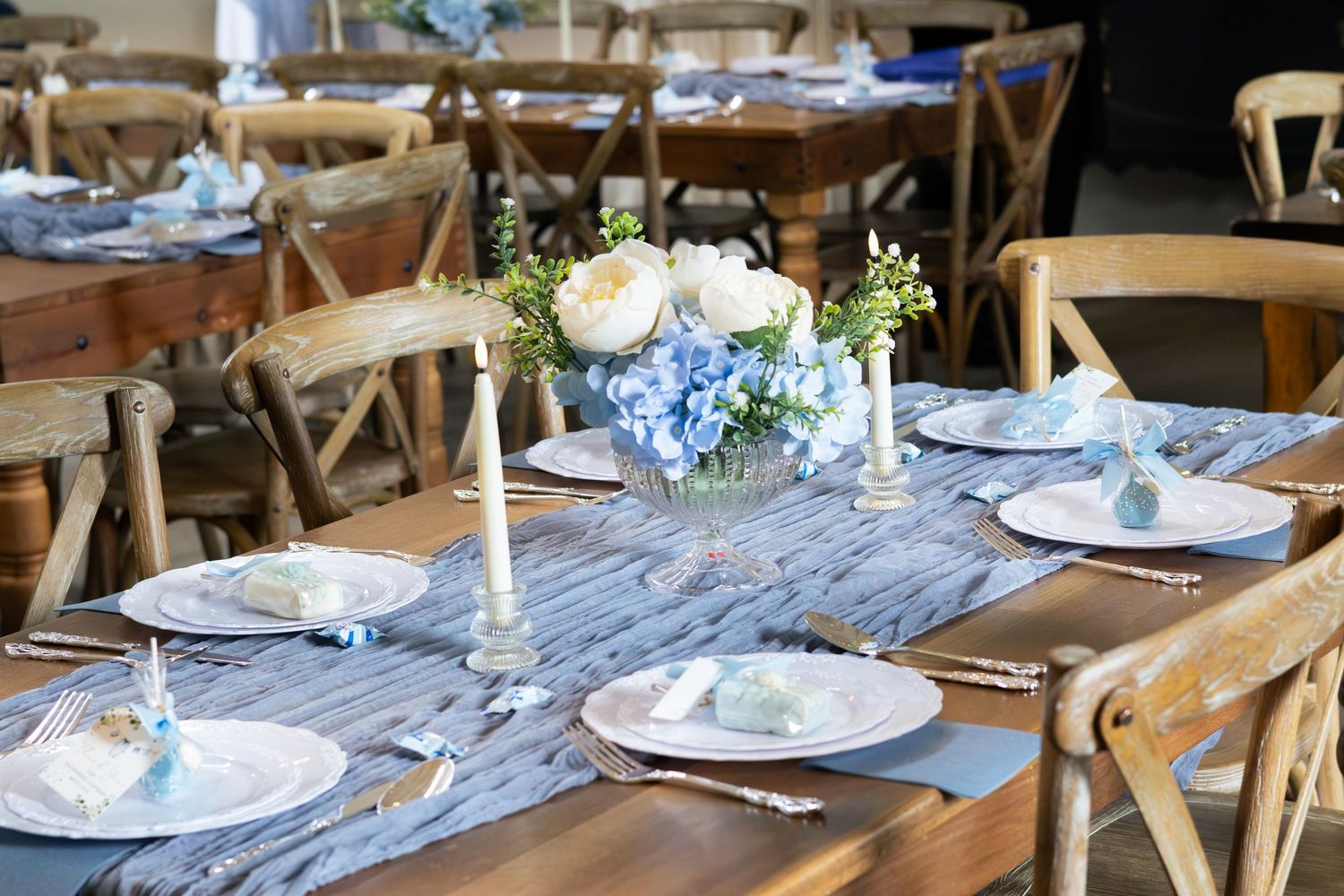 Elegant baby shower table setting with white roses, blue hydrangeas, candles, plates and a blue linen runner.