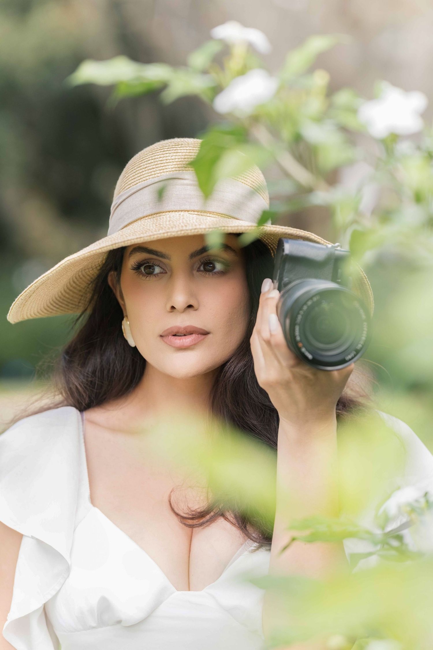 Person wearing a beige sun hat and white blouse poses outdoors in a natural garden setting with camera, london uk photographer.