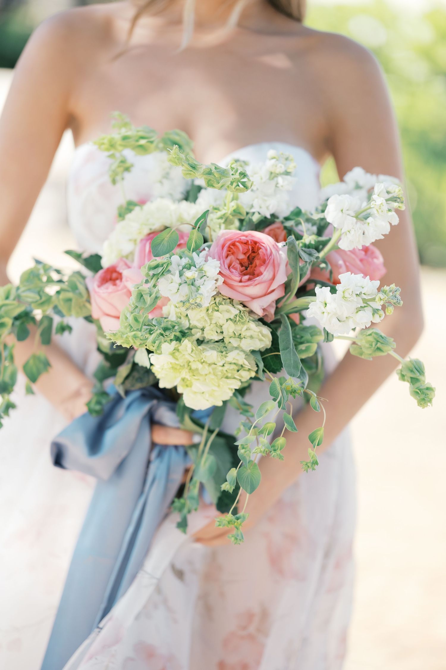 A romantic bridal bouquet with pink garden roses, white hydrangeas and trailing greenery tied with a dusty blue silk ribbon. Wedding UK