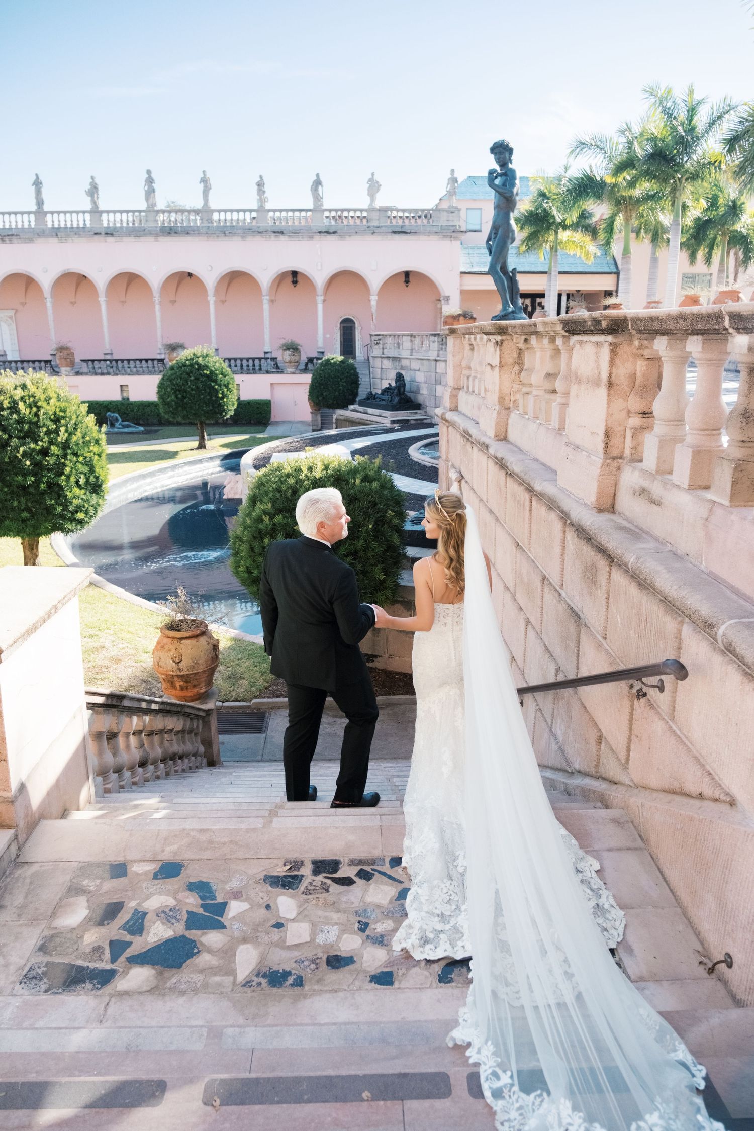A wedding couple poses on an elegant white stone staircase with ornate balustrades at a historic venue. UK wedding photographer.