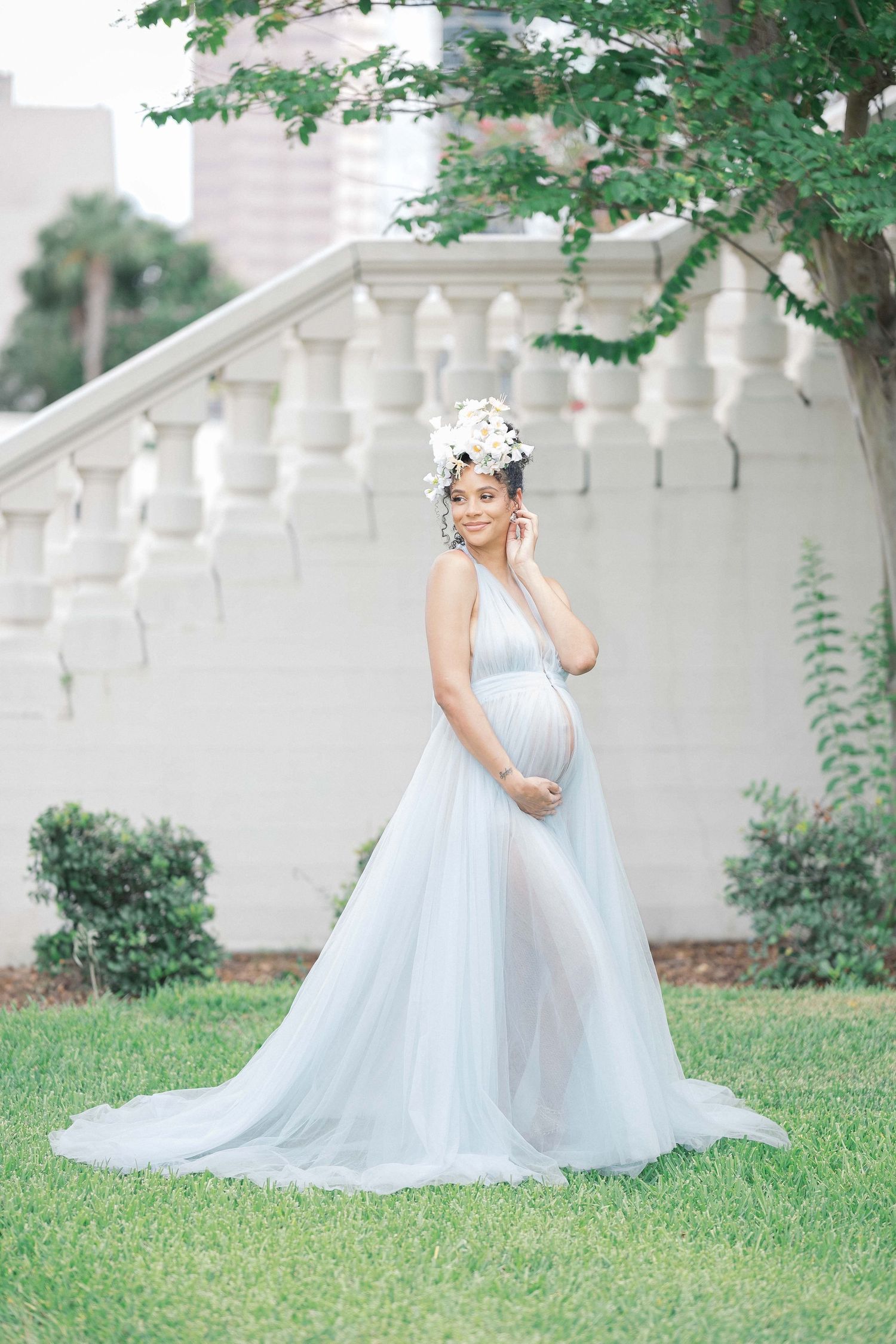 A maternity session in a flowing white gown twirls gracefully on a green lawn beside a white picket fence. Maternity uk photographer.