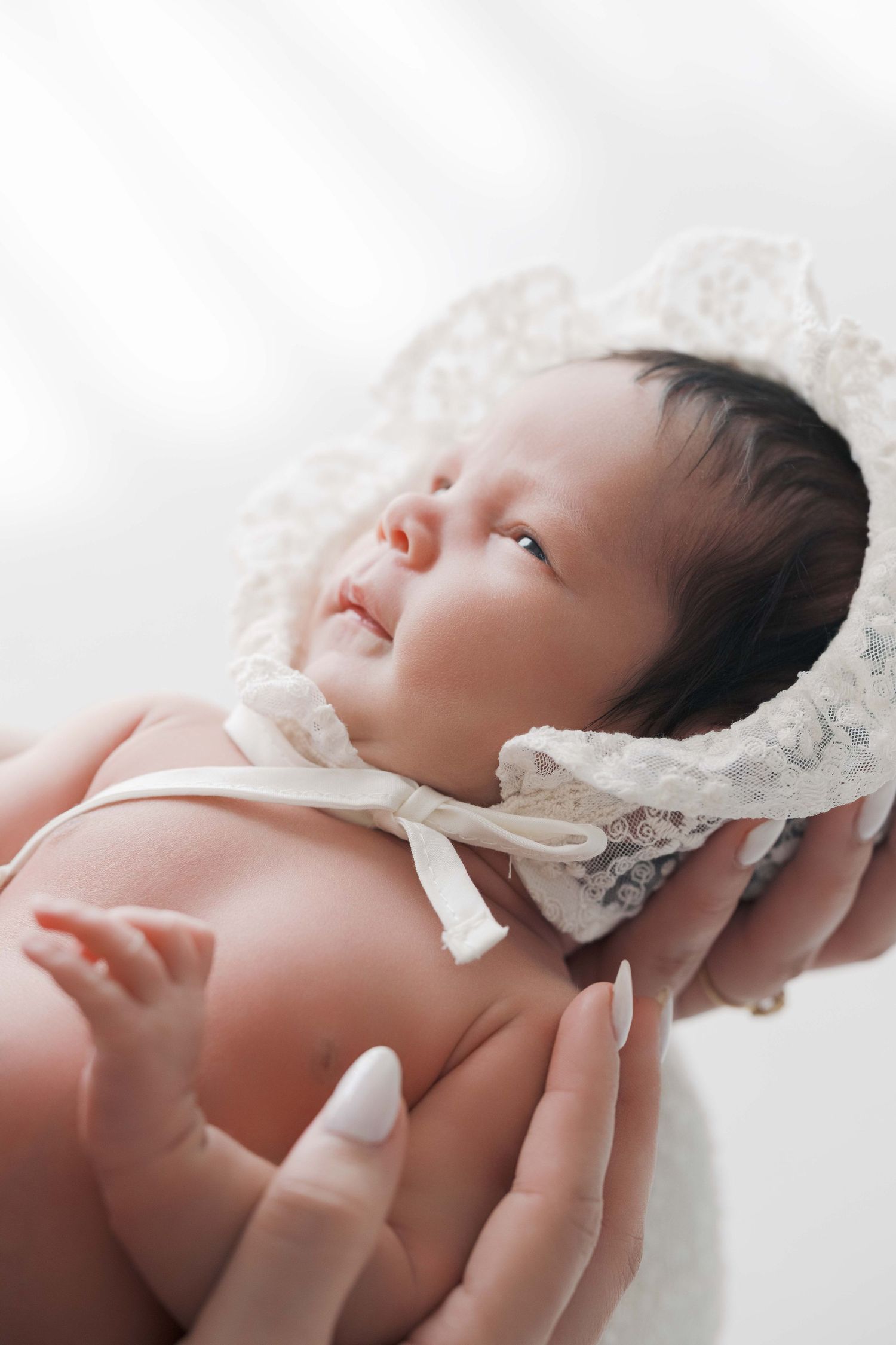 A sleeping newborn baby wrapped in delicate white lace is captured in a series of gentle close-up portraits. london uk