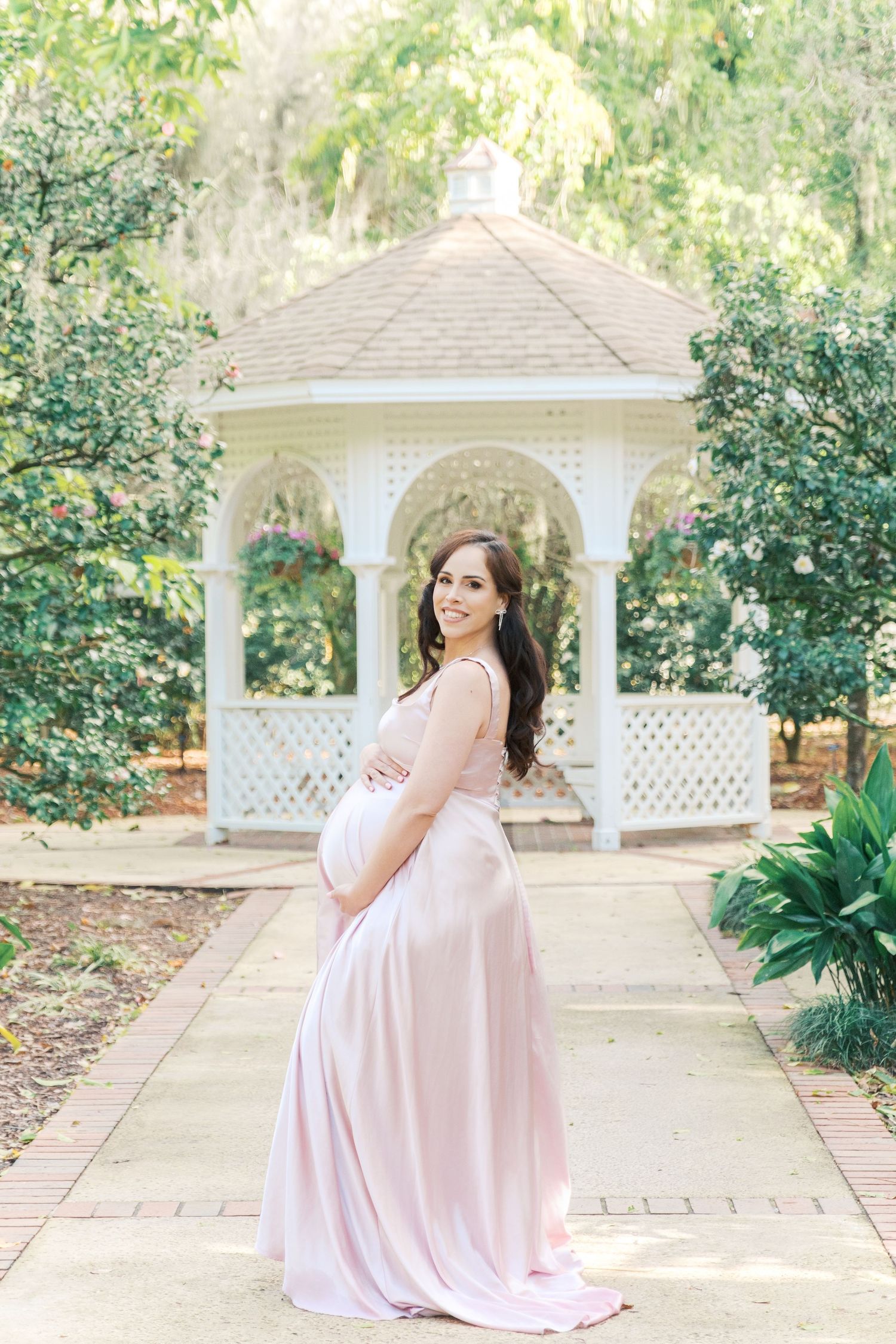 A maternity photo session in a garden gazebo featuring a flowing pink dress and lush greenery background. london uk maternity photographer
