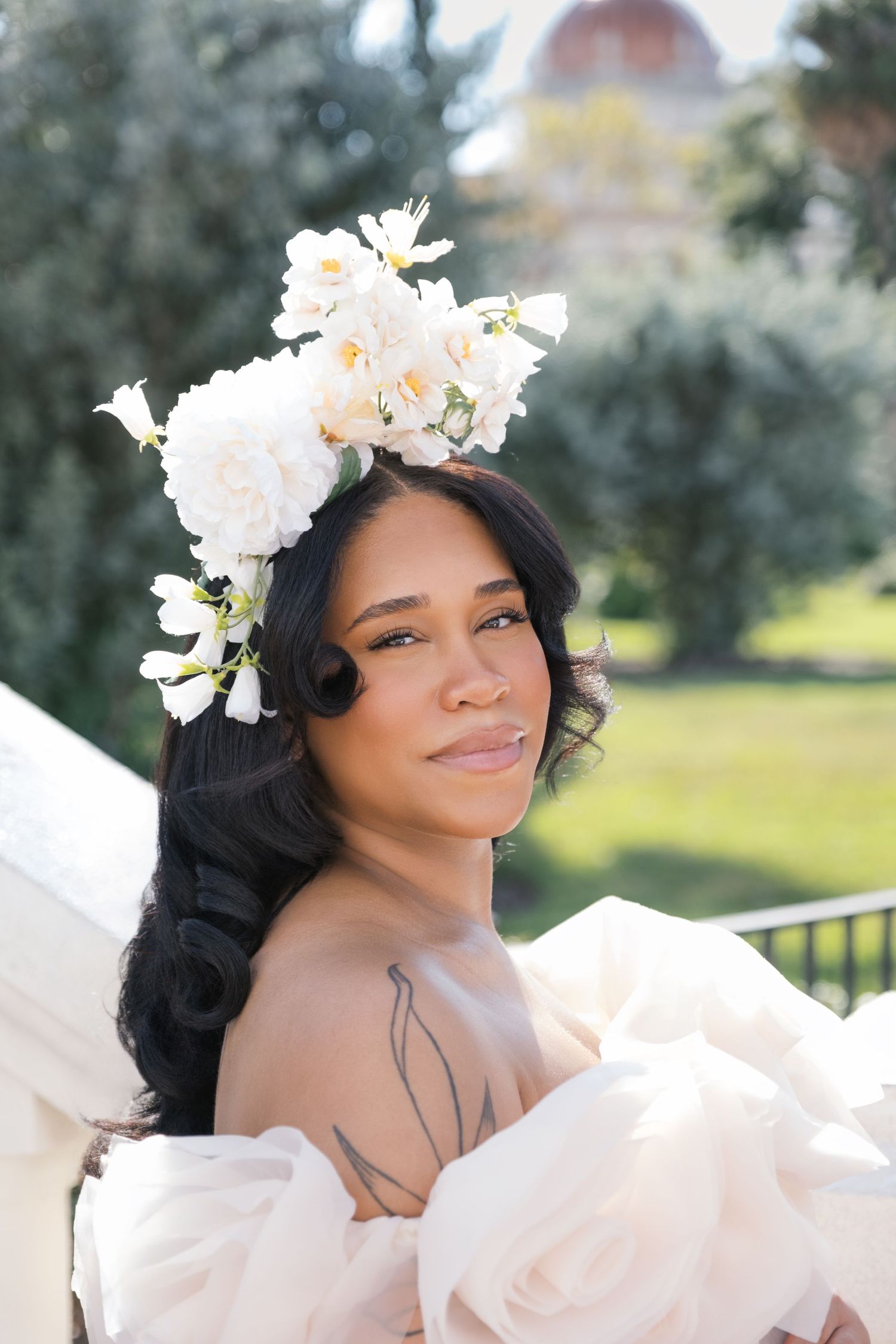 A romantic maternity portrait series featuring delicate white floral crown and flowing ethereal dress in an outdoor garden setting. london