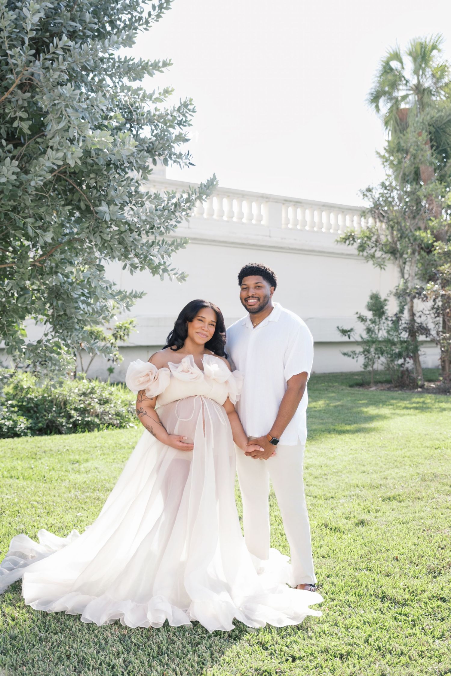 A romantic maternity portrait series featuring delicate white floral crown and flowing ethereal dress in an outdoor garden setting. london