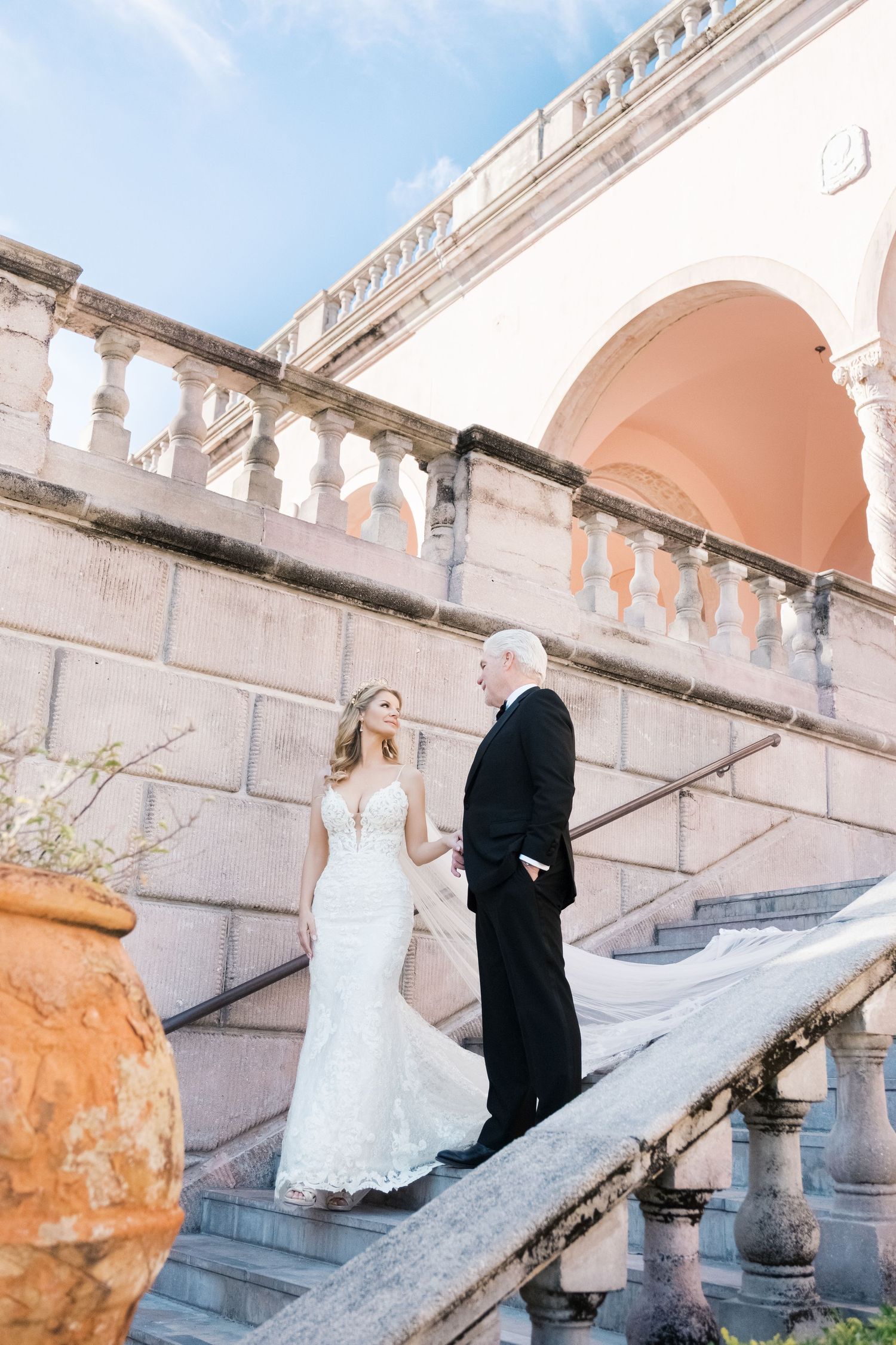 A wedding couple poses on an elegant white stone staircase with ornate balustrades at a historic venue. UK wedding photographer.