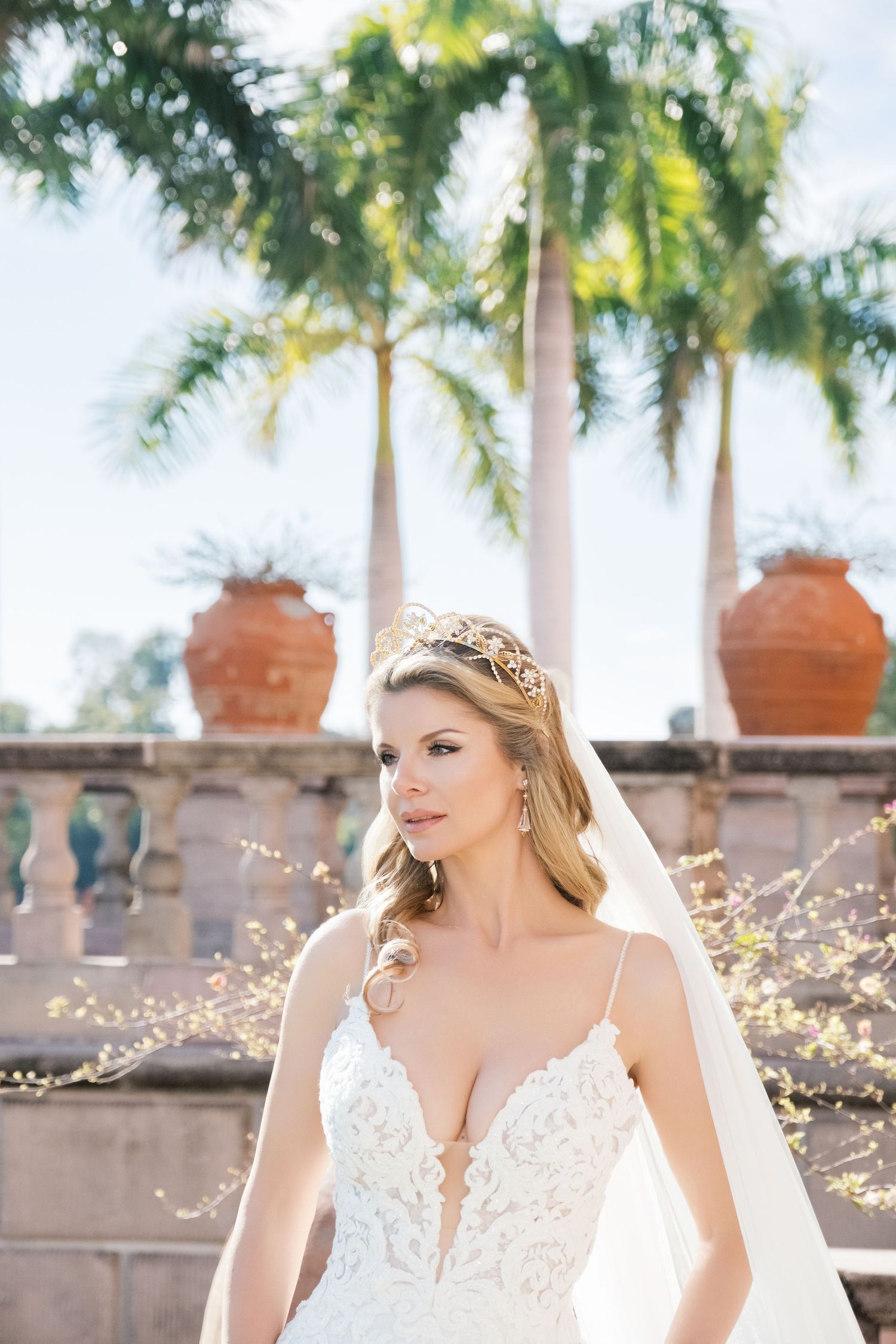 Bride in white wedding dress poses gracefully under Mediterranean-style arches with palm trees and pink flowers. UK wedding photographer