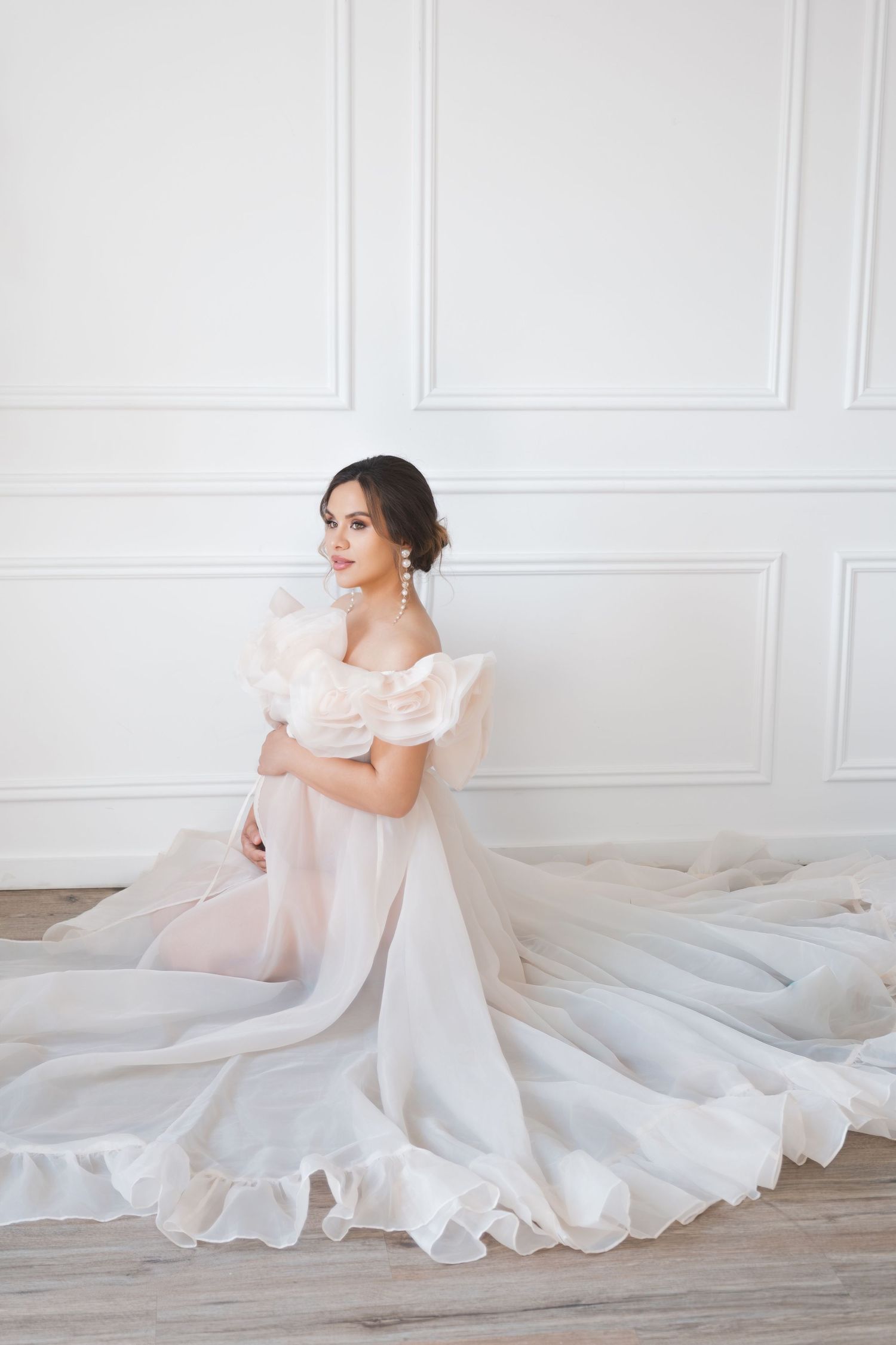 A expecting mum in a flowing white wedding dress poses elegantly against a white wall in a series of romantic portraits. london uk shoot