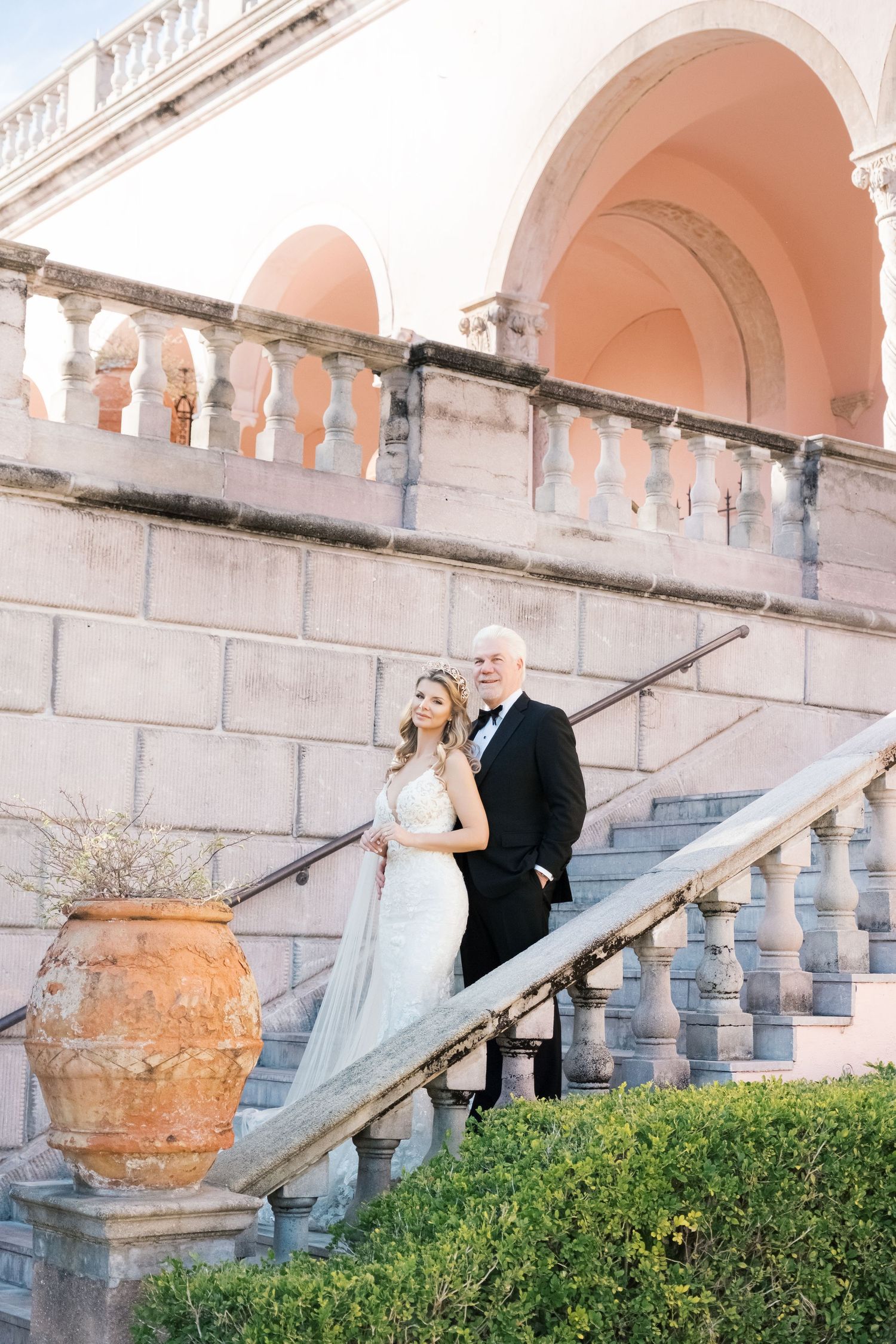 A wedding couple poses on an elegant white stone staircase with ornate balustrades at a historic venue. UK wedding photographer.
