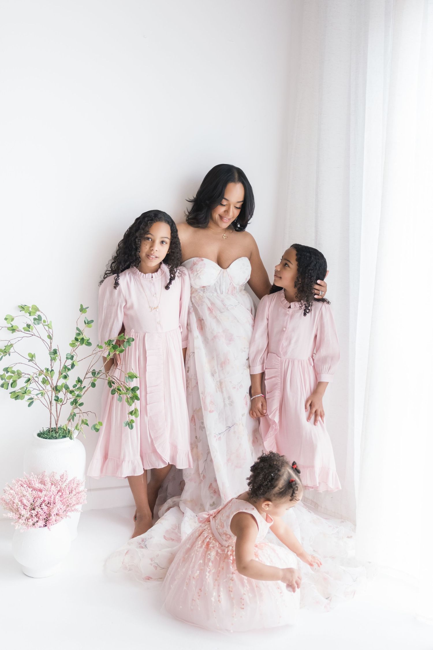 A sweet family photoshoot featuring matching white and pink dresses against a light background. Motherhood photographer london, uk.