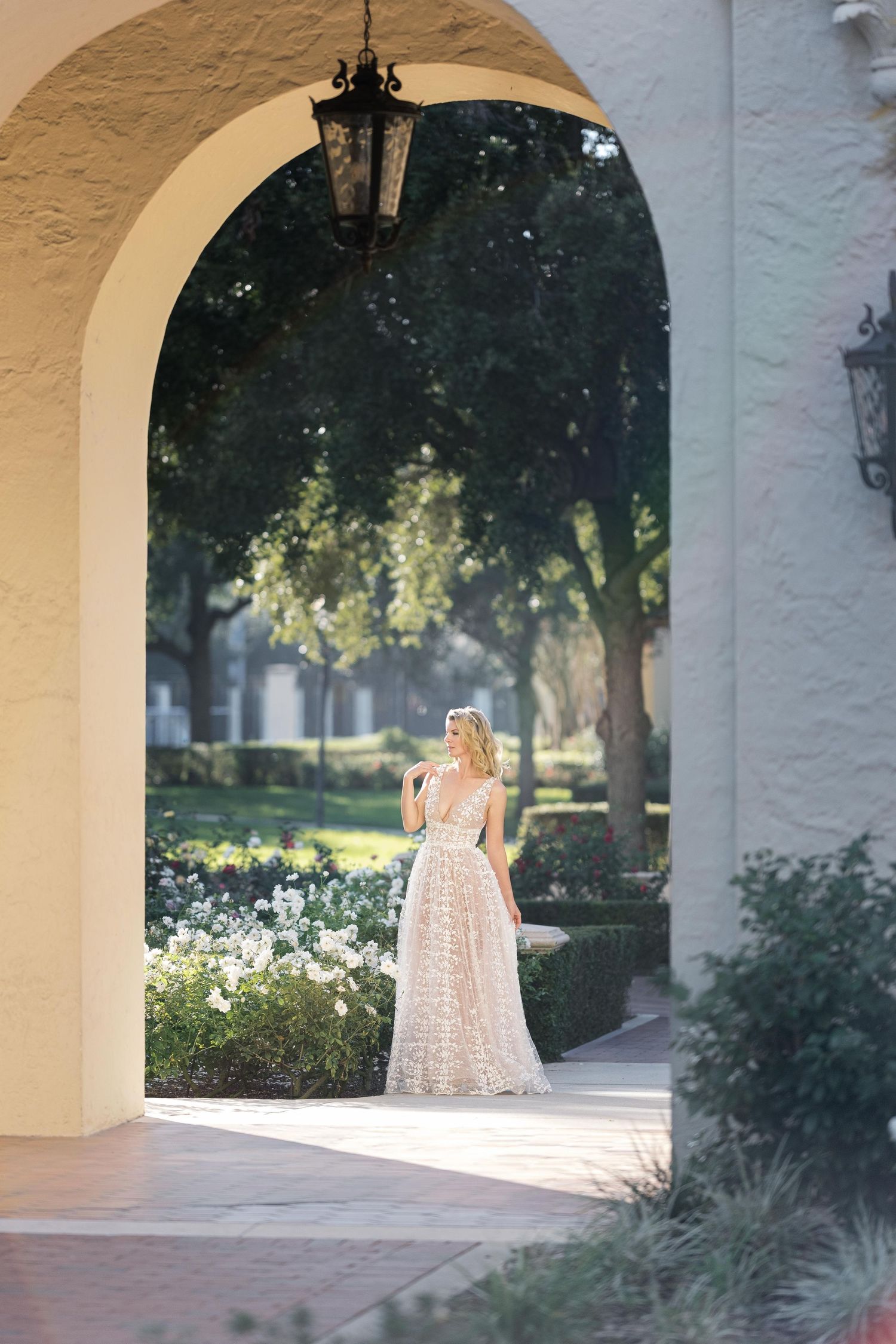 Sunlit arched walkway in a Mediterranean-style building with white columns and garden views through the openings. Motherhood UK photographer