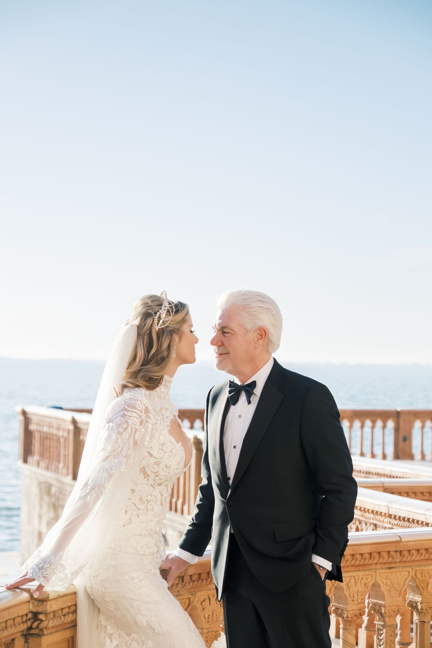 Elegant couple in wedding attire share intimate moments on ornate balcony overlooking ocean at sunset. cambridge uk photographer.