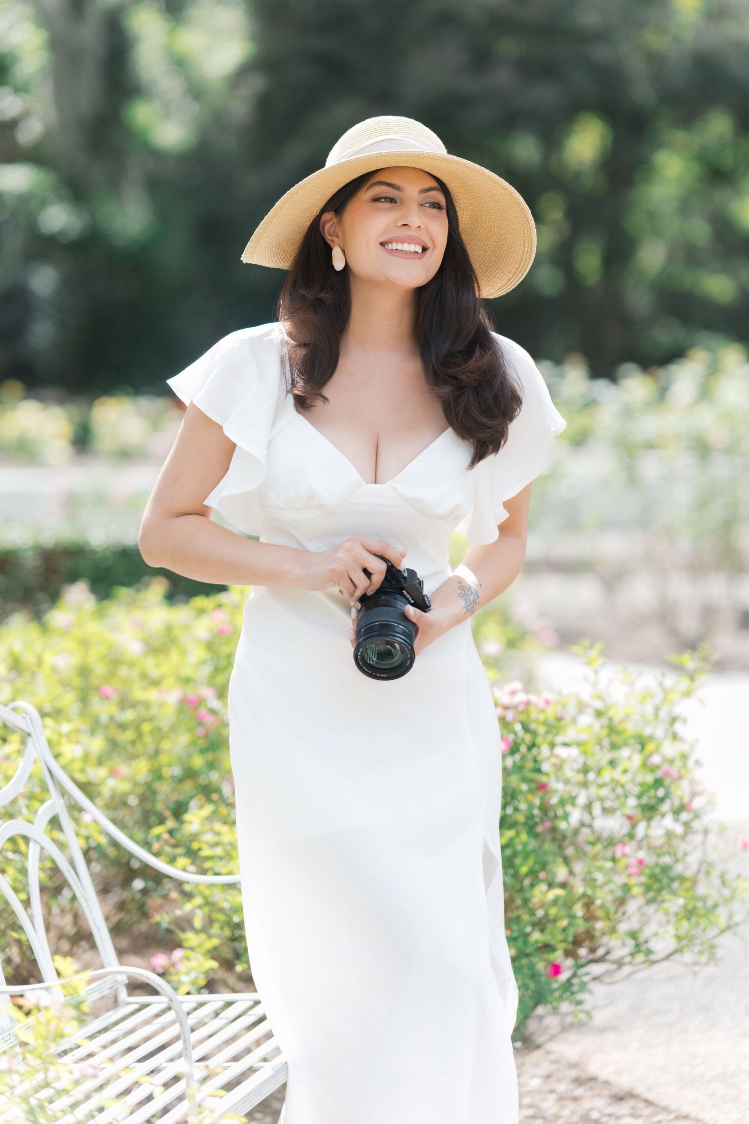 Person in white summer dress and straw hat holding camera in sunny garden setting. editorial motherhood london uk photographer.