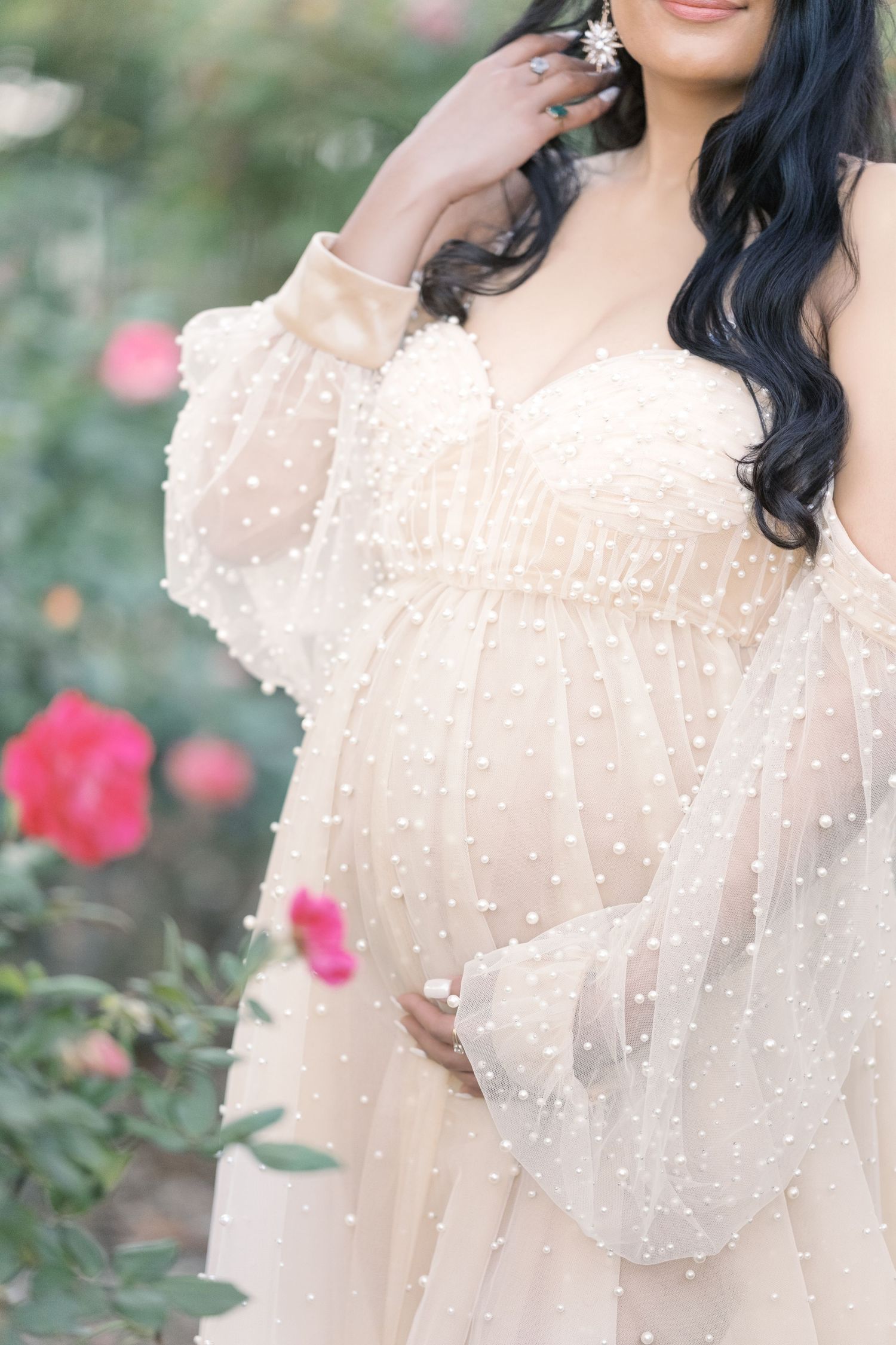 A maternity belly pearl dress with ruffled details and sheer sleeves photographed in a garden setting. Maternity Photographer cambridge
