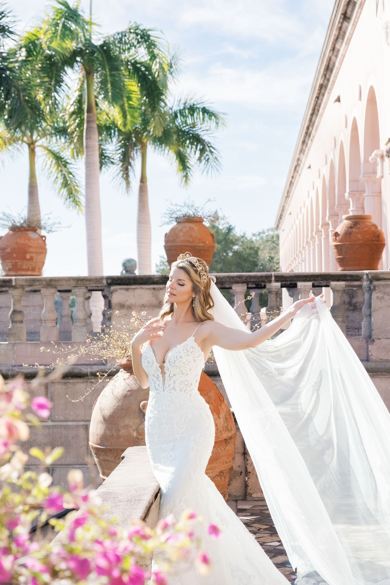 Bride in white wedding dress poses gracefully under Mediterranean-style arches with palm trees and pink flowers. UK wedding photographer