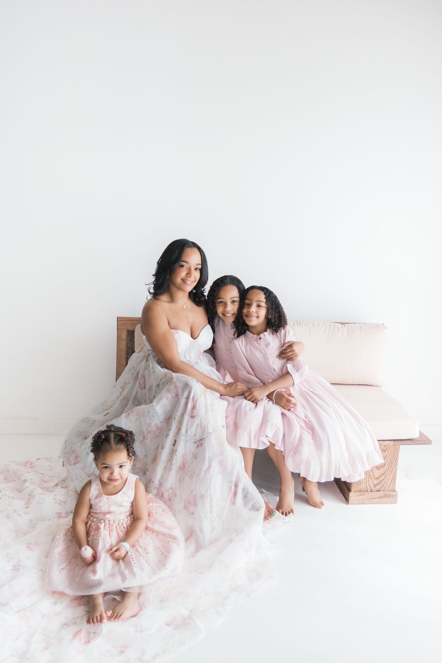 A sweet family photoshoot featuring matching white and pink dresses against a light background. Motherhood photographer london, uk.