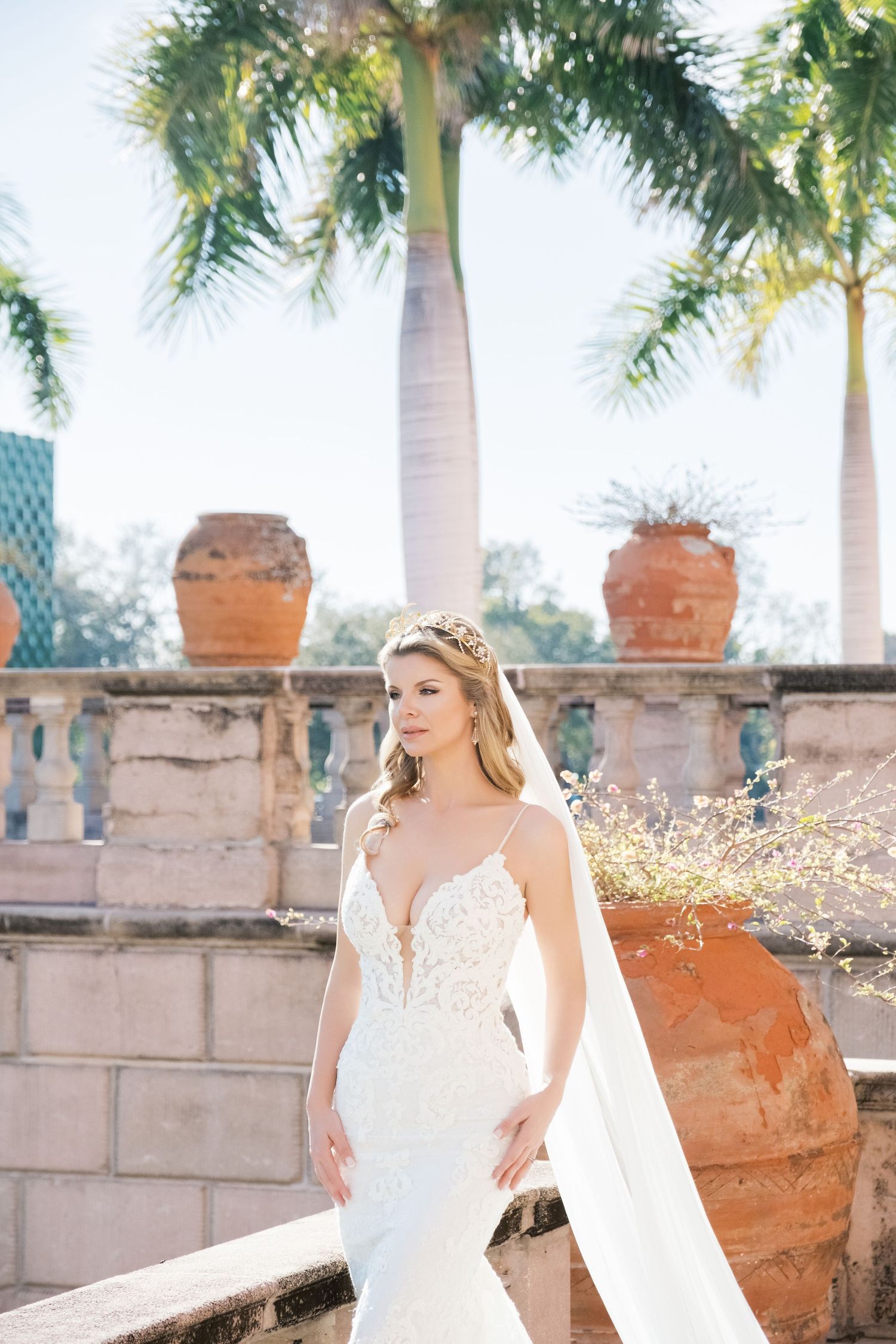 Bride in white wedding dress poses gracefully under Mediterranean-style arches with palm trees and pink flowers. UK wedding photographer