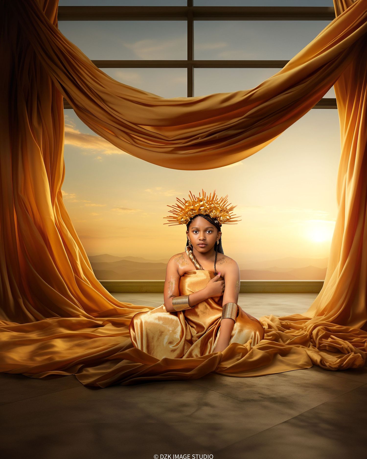 Young girl wearing a golden sunburst crown and satin gown sits on a draped floor before a glowing sunset window.