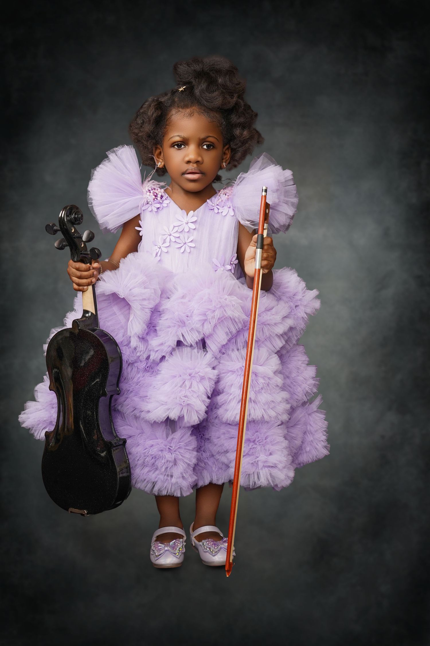 Young girl in a lavender ruffled tulle dress holds a black violin and bow while standing against a dark green studio backdrop.