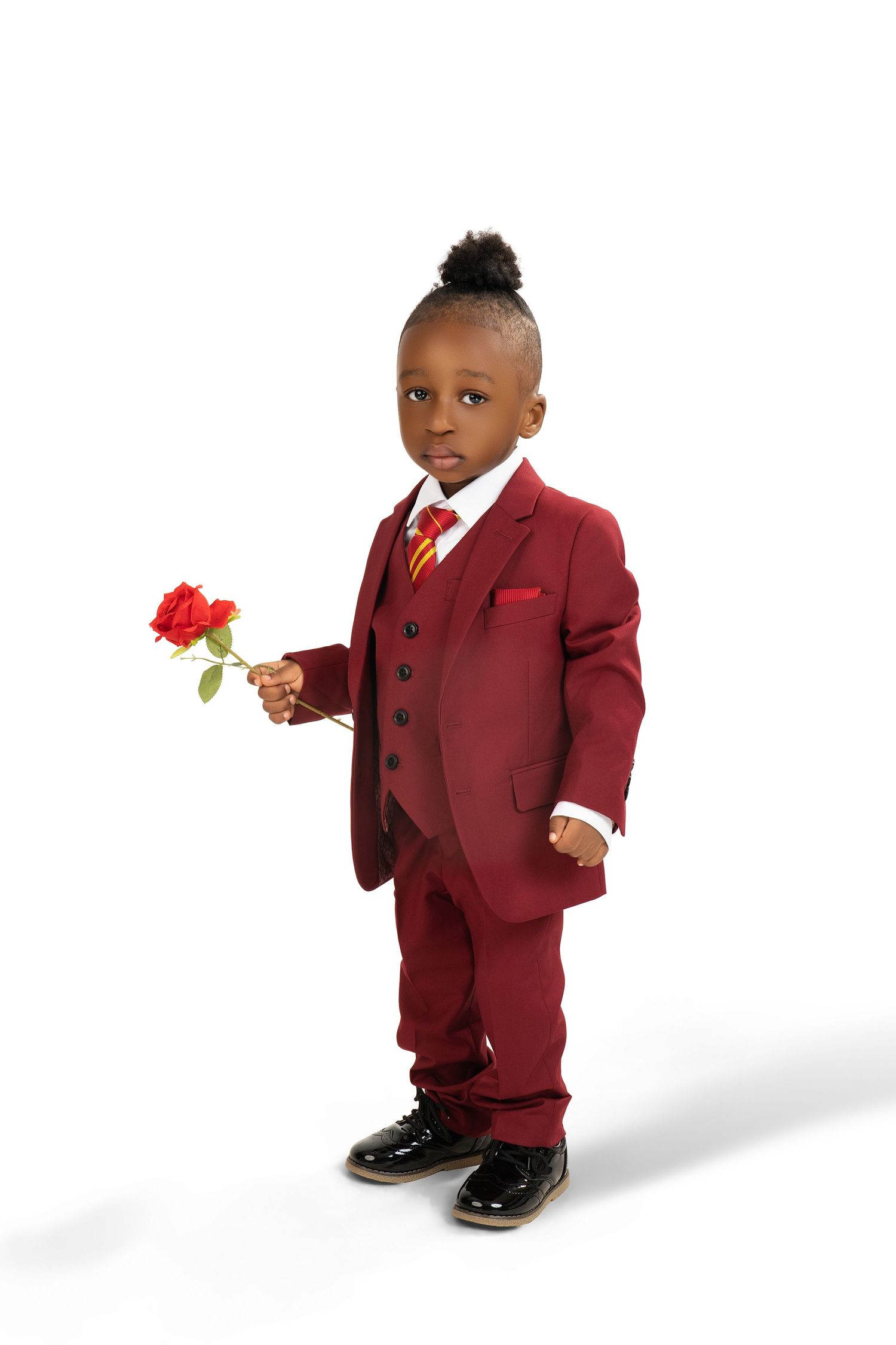 Toddler boy in a burgundy three-piece suit and striped tie holds a red rose in a classic studio portrait.