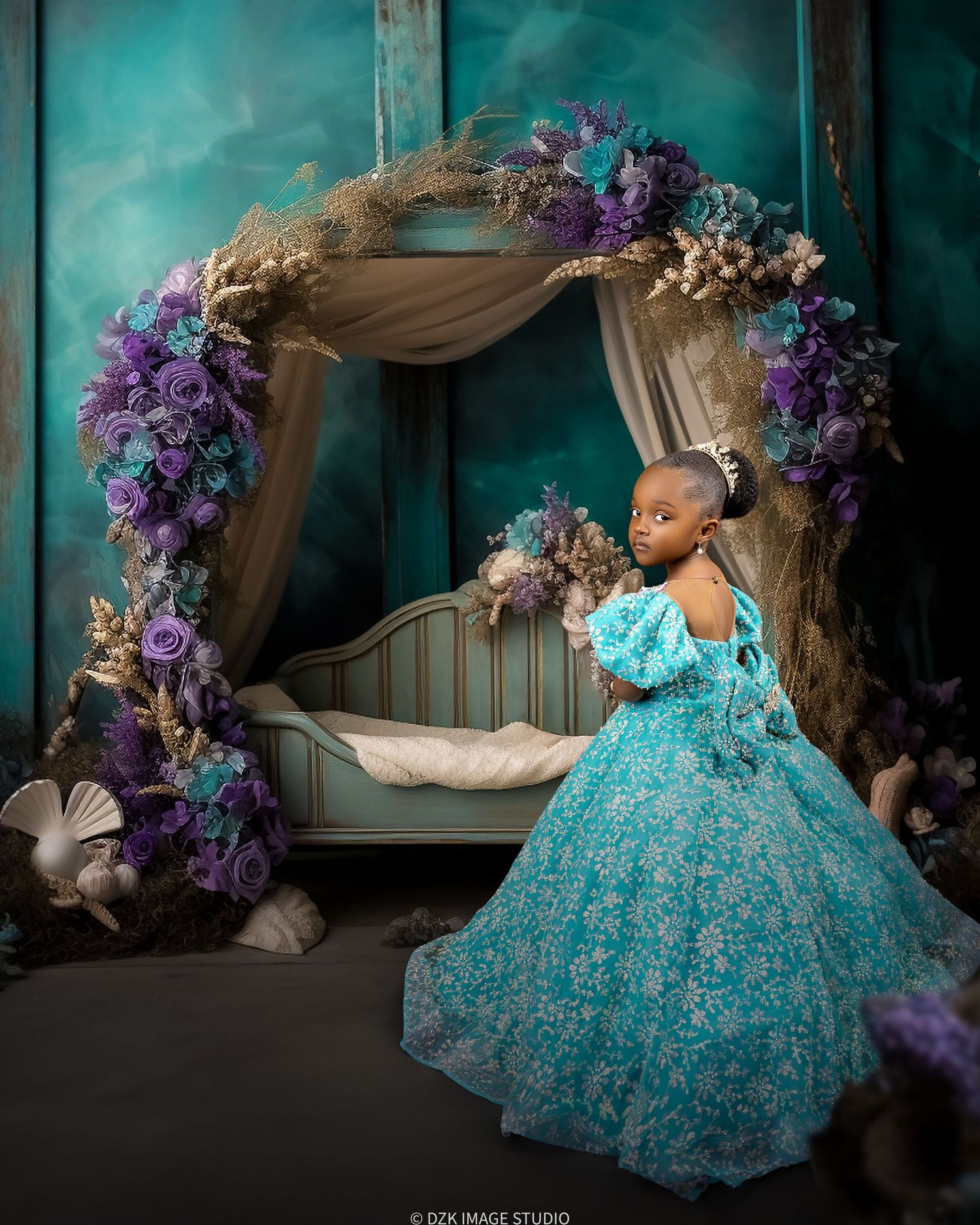 Girl in a teal lace ball gown stands beside a floral arch and canopy bed in a moody turquoise fantasy studio scene.