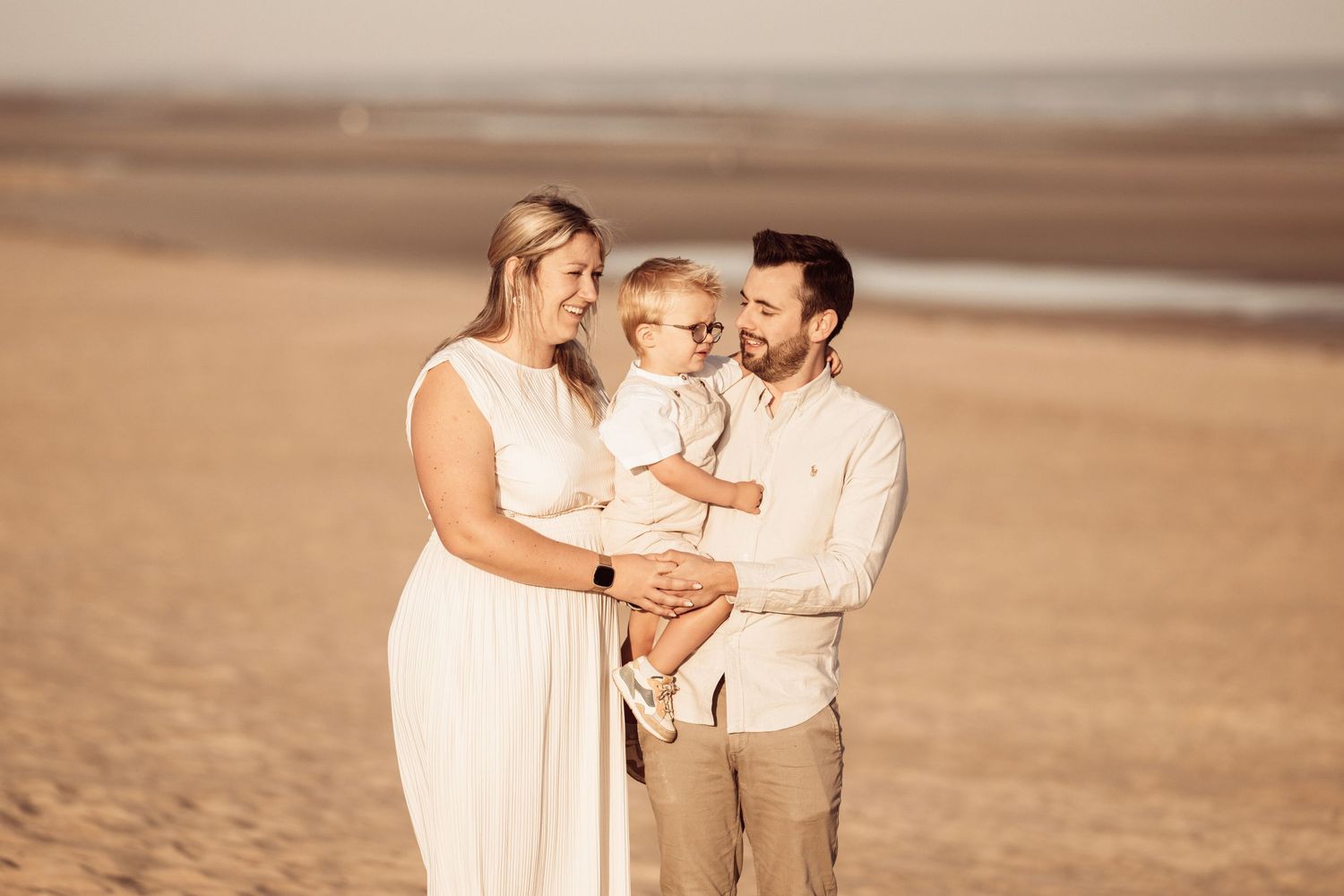 A family shares a tender moment together on a sandy beach at sunset in soft warm lighting.