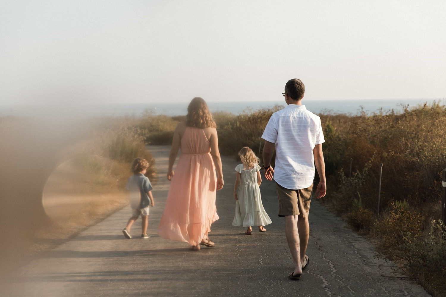 Family of four walking together on a misty coastal path at golden hour near the ocean.