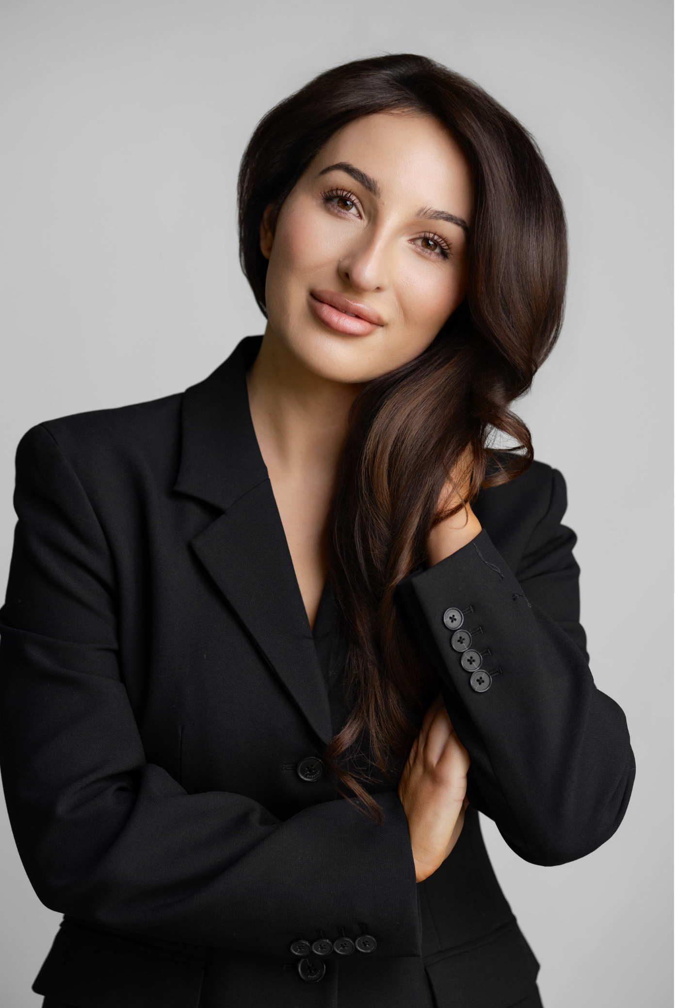 Professional woman in black blazer posing confidently against a neutral background.