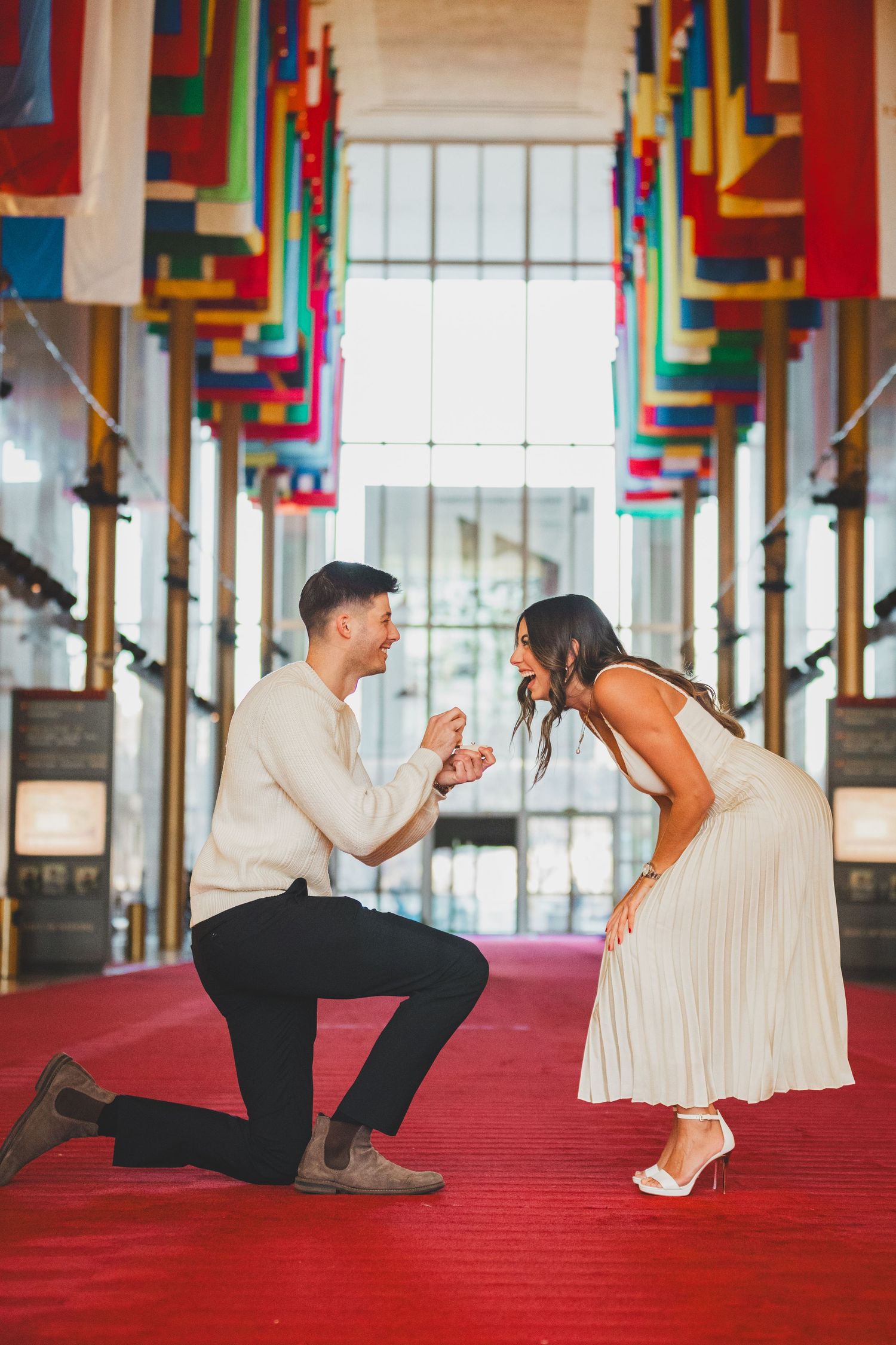 Proposal scene on red carpet with colorful geometric ceiling and columns.