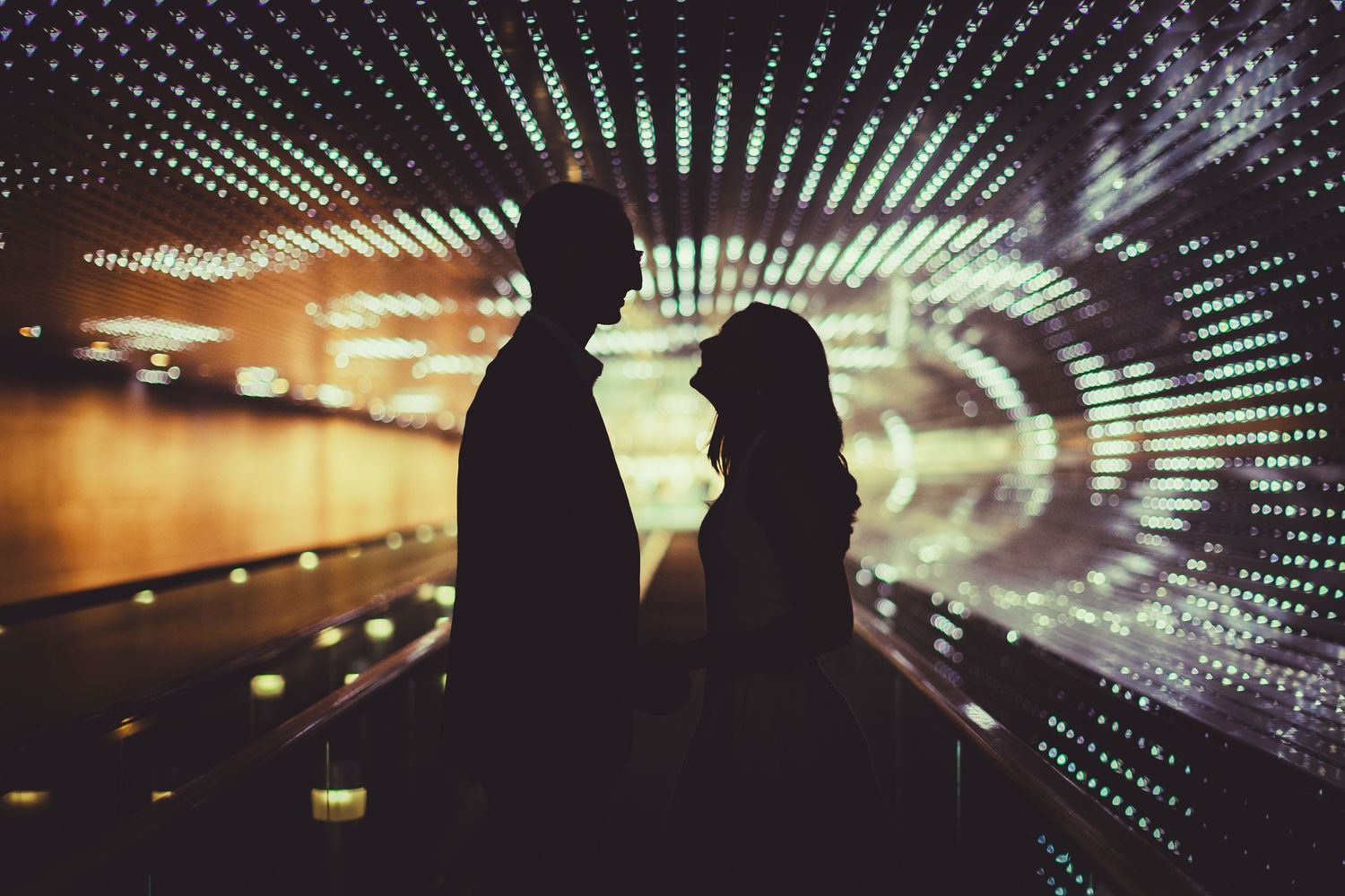 Romantic silhouette of a couple facing each other in a glowing tunnel with bokeh lights in the background.