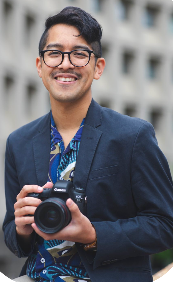 Stefan A. Photography, a Washington DC photographer,  in navy blazer and patterned shirt smiles while holding Canon DSLR camera outdoors.