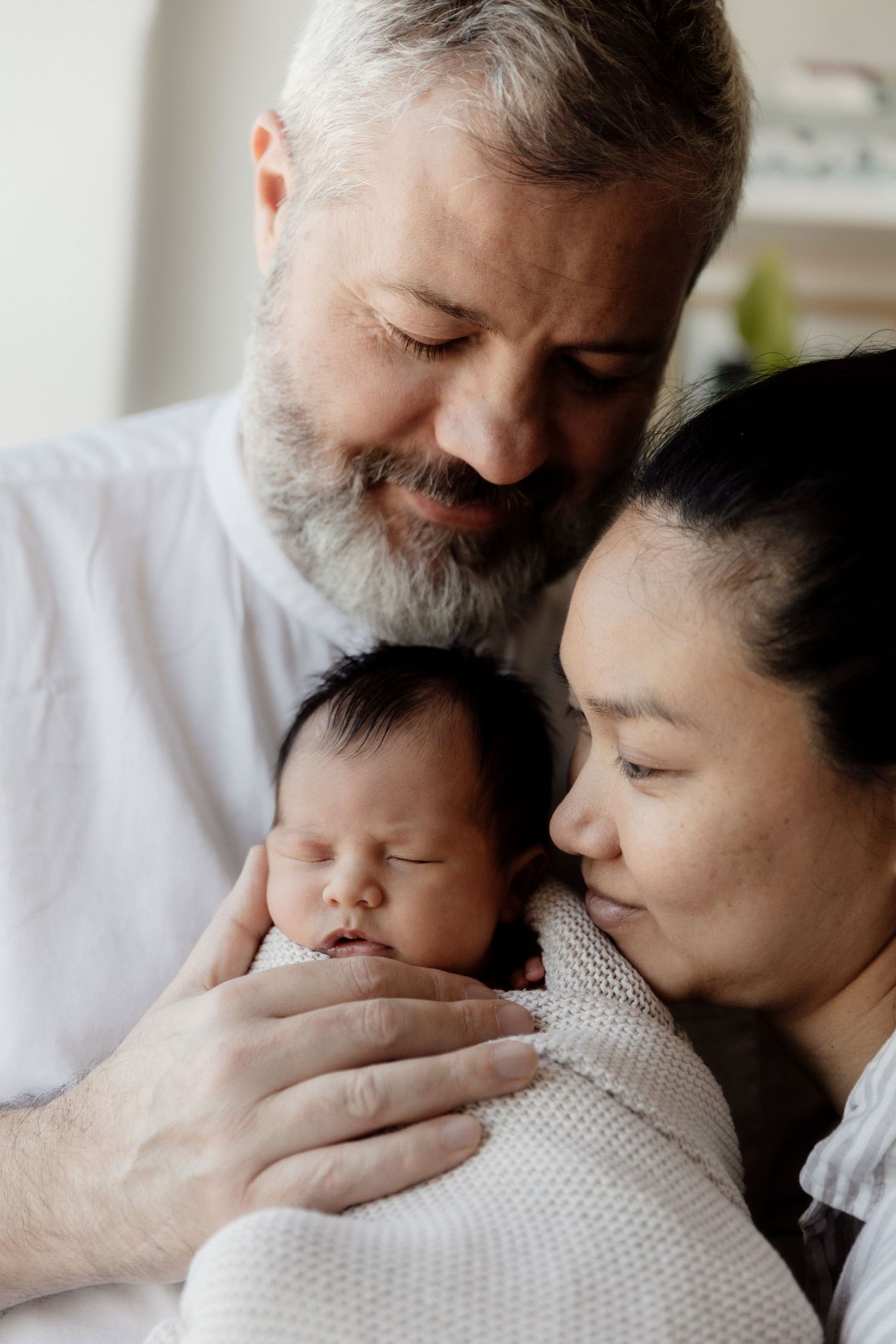 Older man and a woman cradling a sleeping newborn close to their faces