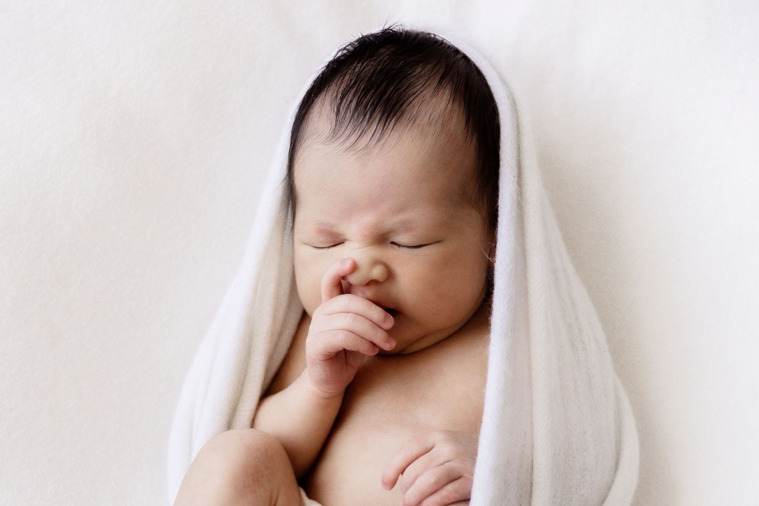 Close-up of a newborn baby's face wrapped in white, photographed at home