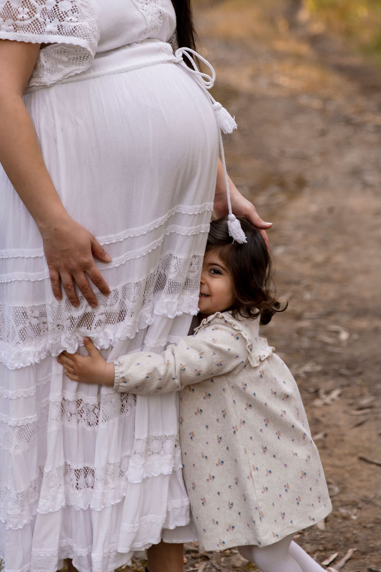 Pregnant mother outdoors at golden hour with her young daughter holding her dress
