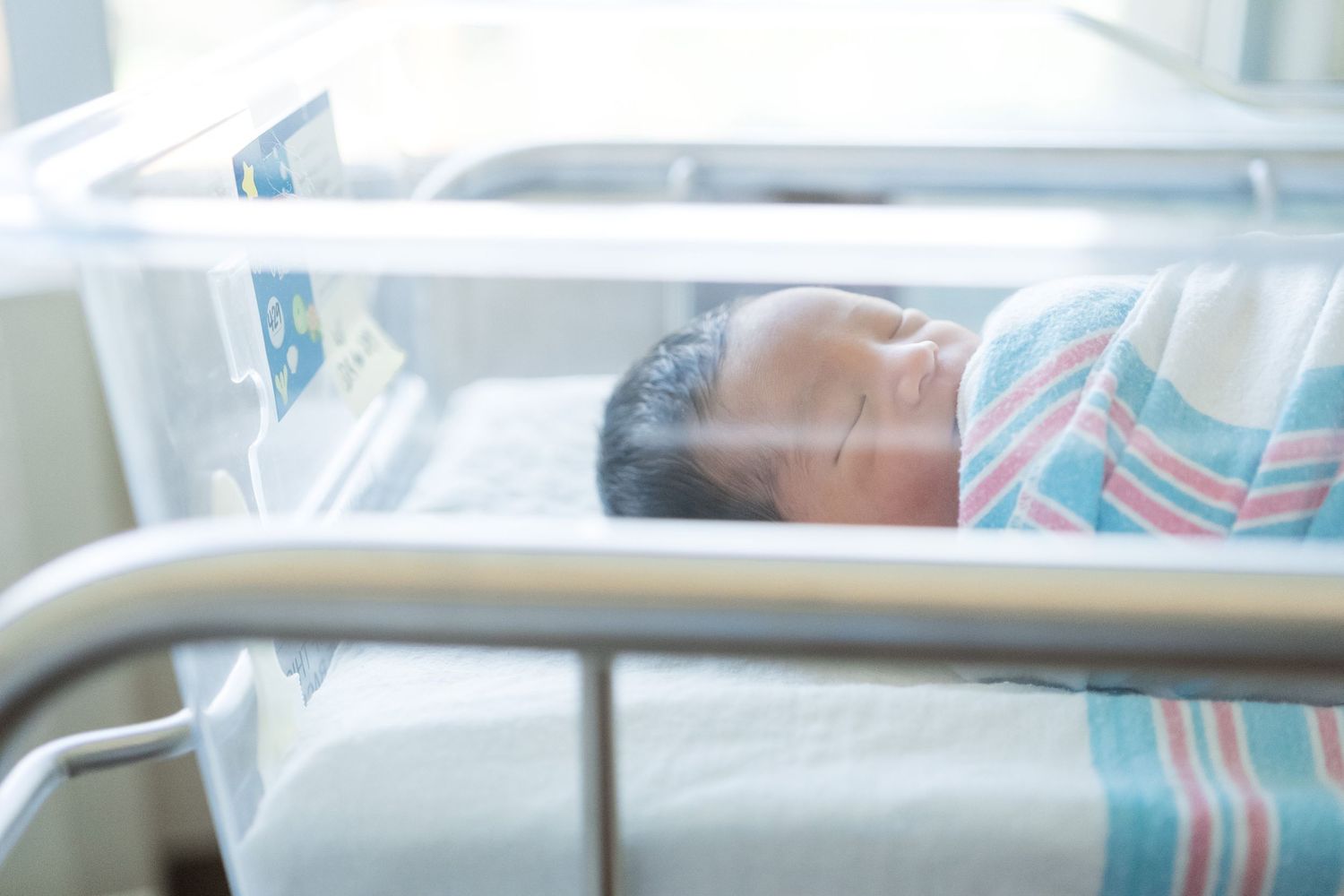 A newborn baby sleeps peacefully in a hospital bassinet with protective metal rails.