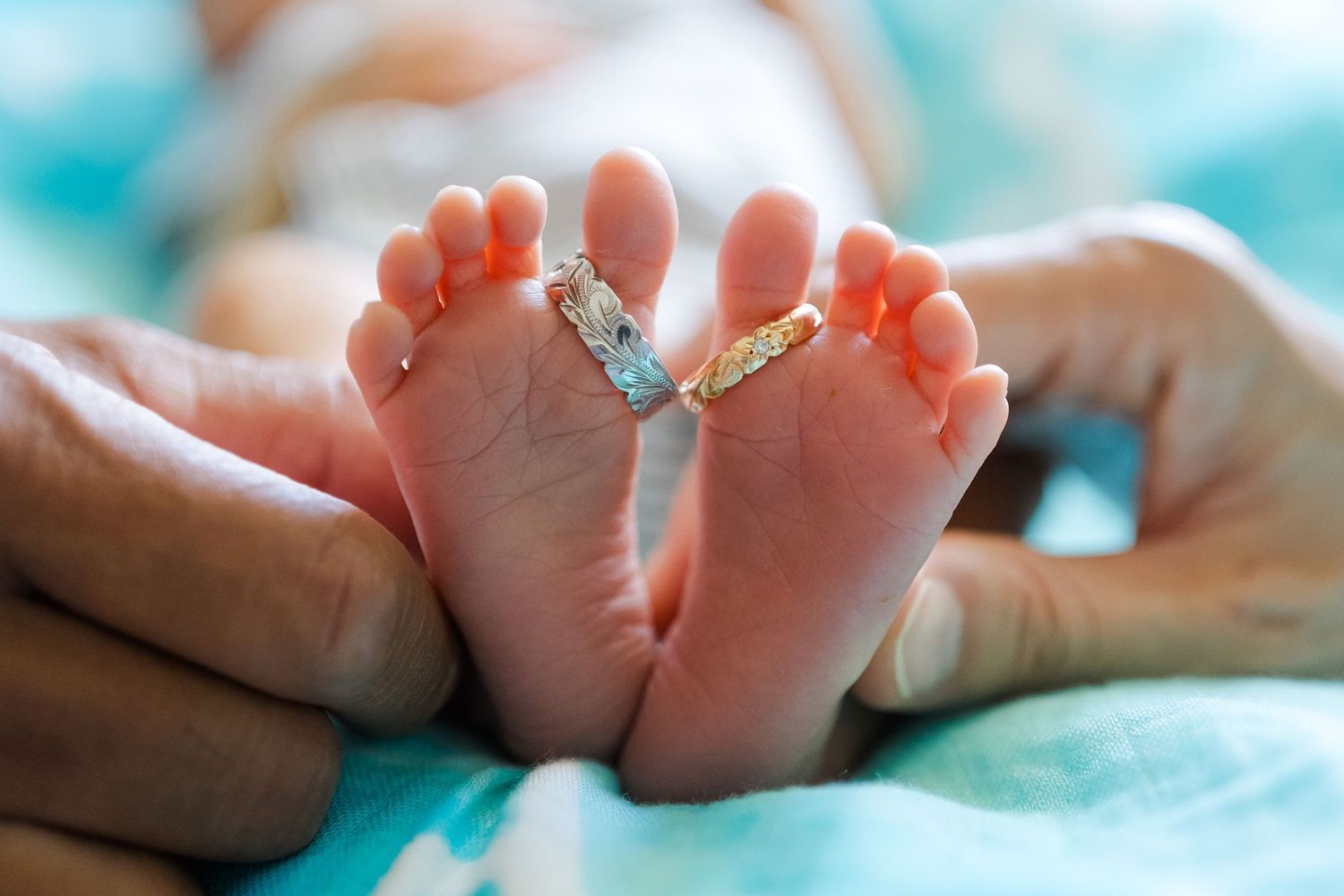 Tiny baby feet with wedding rings placed between the toes against a turquoise background. Oahu Newborn Photographer