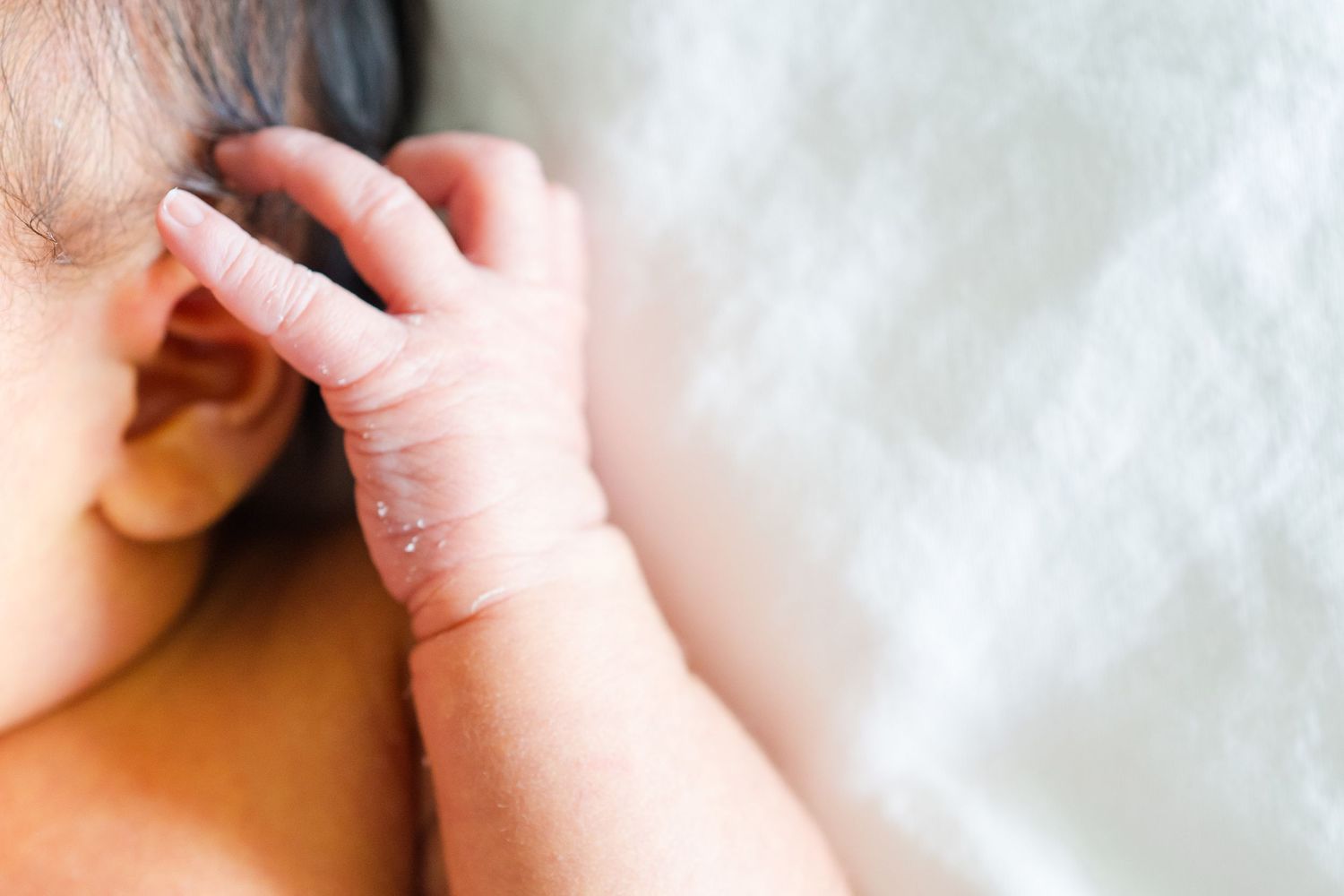 Close-up of a tiny infant hand near mouth against white background.　Oahu Newborn Photographer