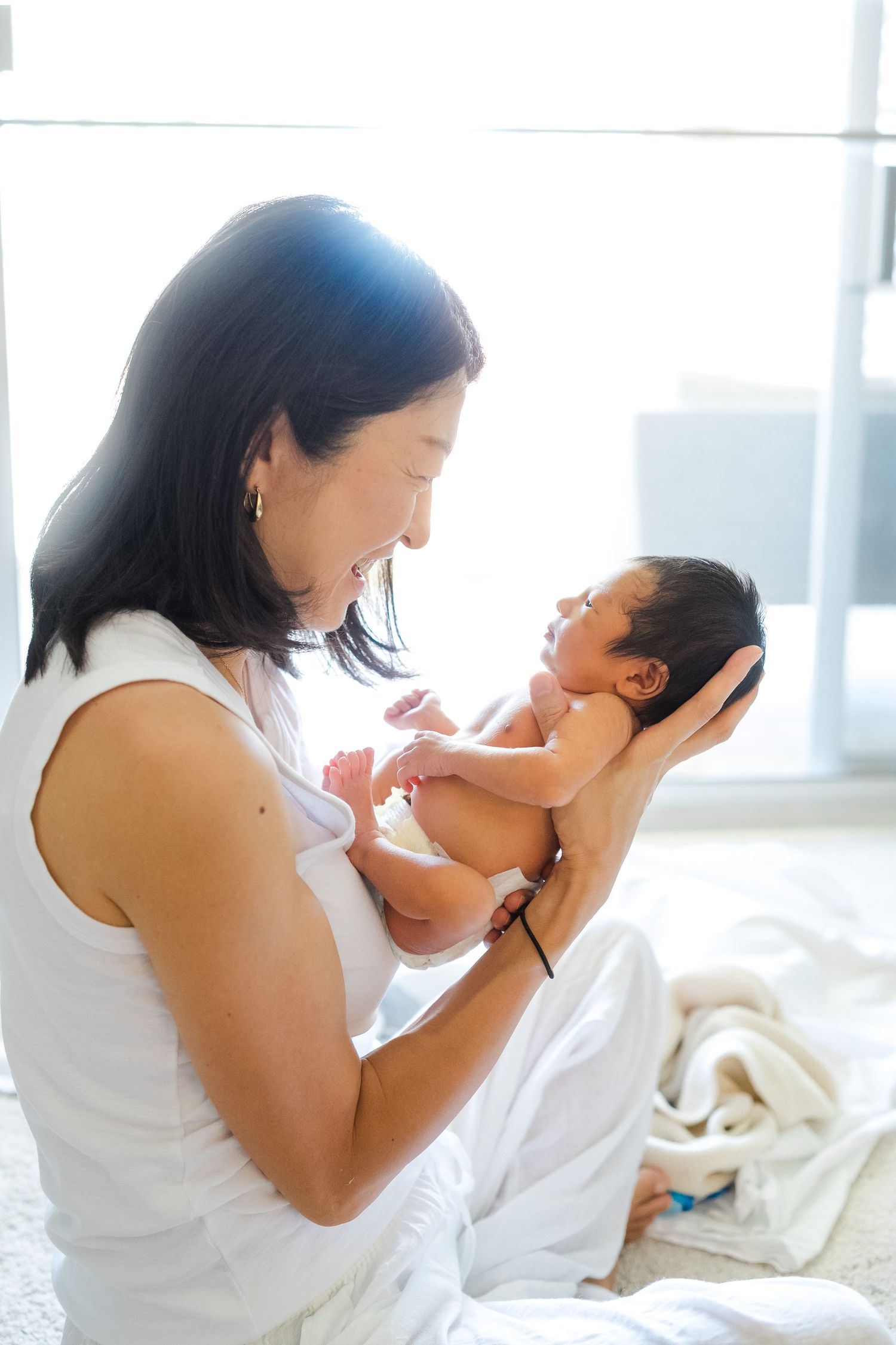 A tender moment between a parent and newborn baby in a bright, sunlit room. Oahu Newborn Photographer