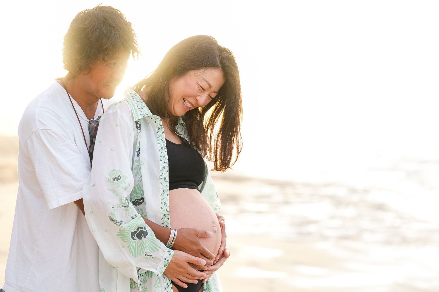 Expectant couple embraces on sunny beach during maternity photoshoot with backlit glow at golden hour.
oahu maternity photo