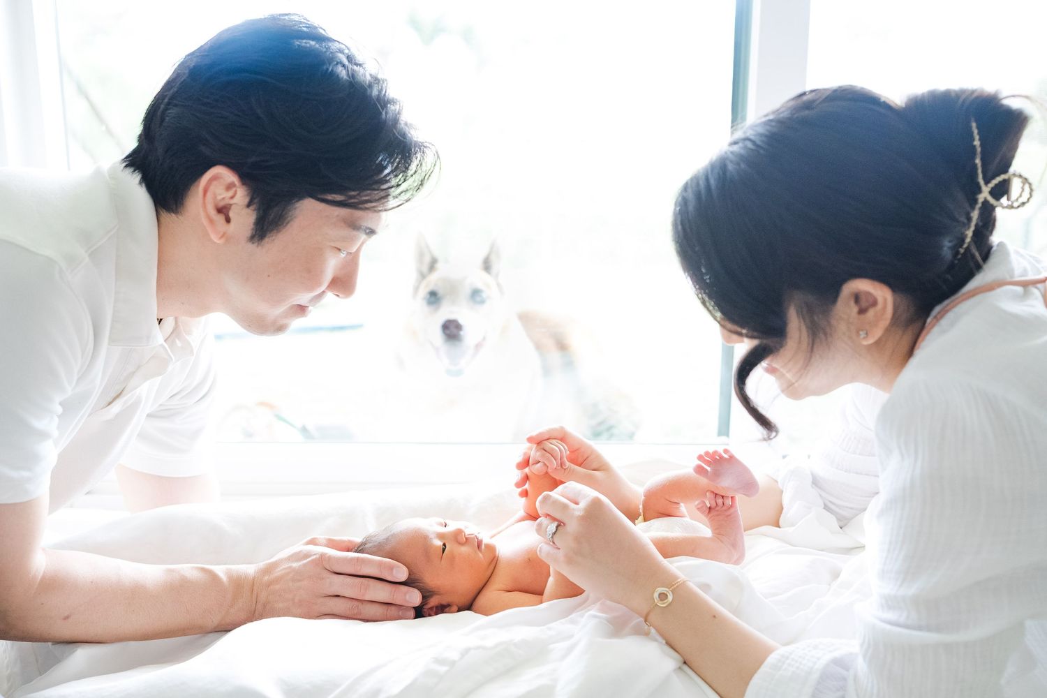 Parents dressing and caring for their newborn baby in white room with sunlight streaming through window. Oahu Newborn Photographer