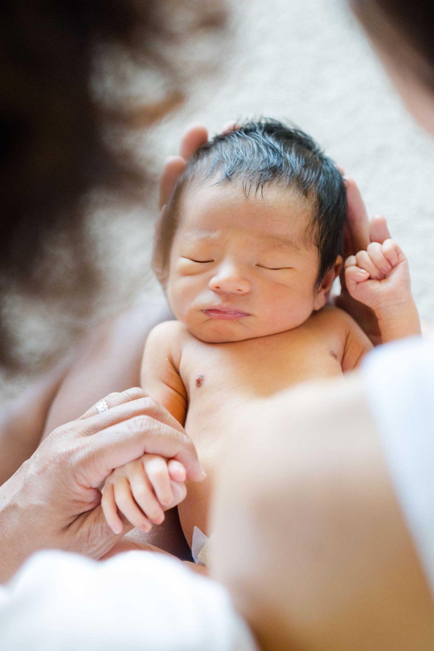 A peaceful sleeping newborn baby rests in loving hands with dark hair and closed eyes. Oahu Newborn Photographer