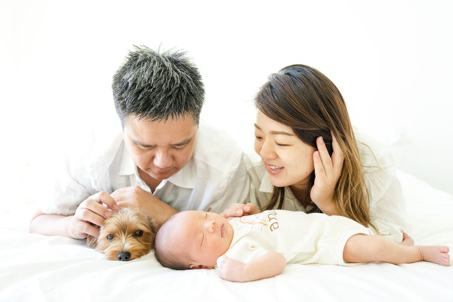 A loving family relaxing together with their dog and baby on a white bed.Oahu Newborn Photographer