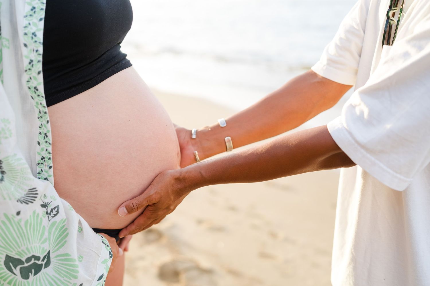 Medical care provider examines pregnant woman's belly during a prenatal checkup at an outdoor location. oahu maternity photo