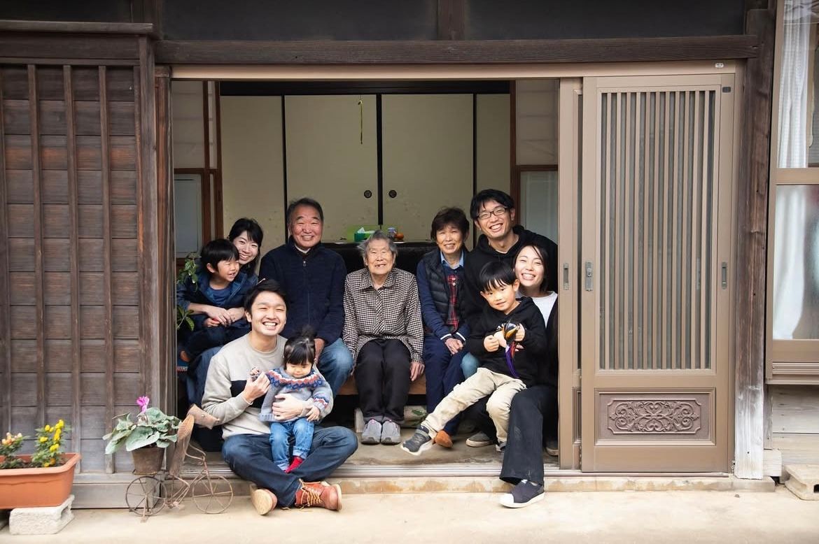 A group of people sitting together on the steps of a traditional Japanese house entrance.