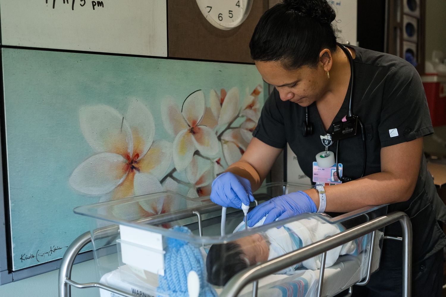 Medical professional wearing blue gloves performs care procedures on mobile medical cart with floral artwork in background.