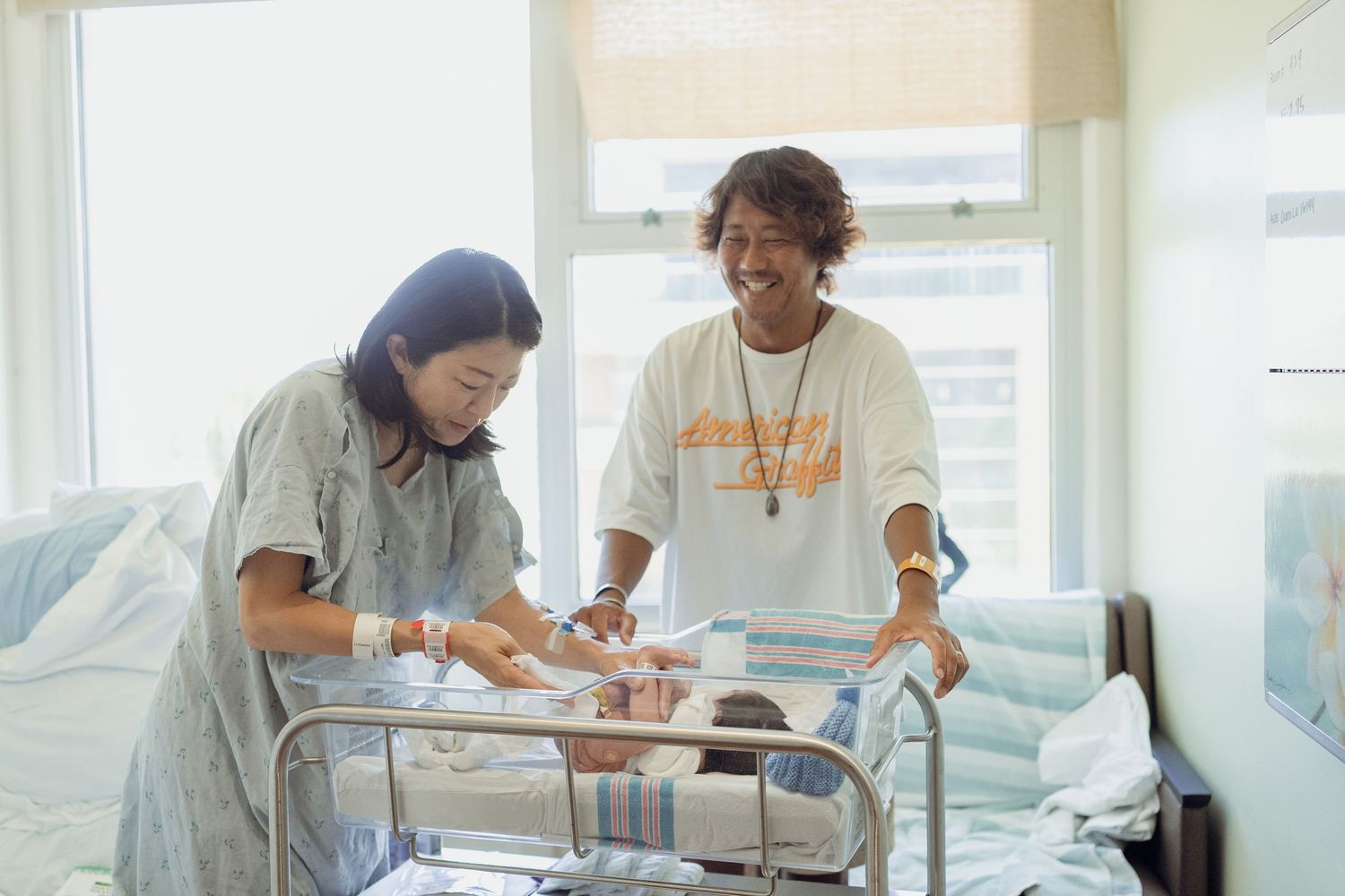 Two healthcare workers attentively examine a medical cart with supplies in a brightly lit hospital room.　Oahu Newborn Photographer