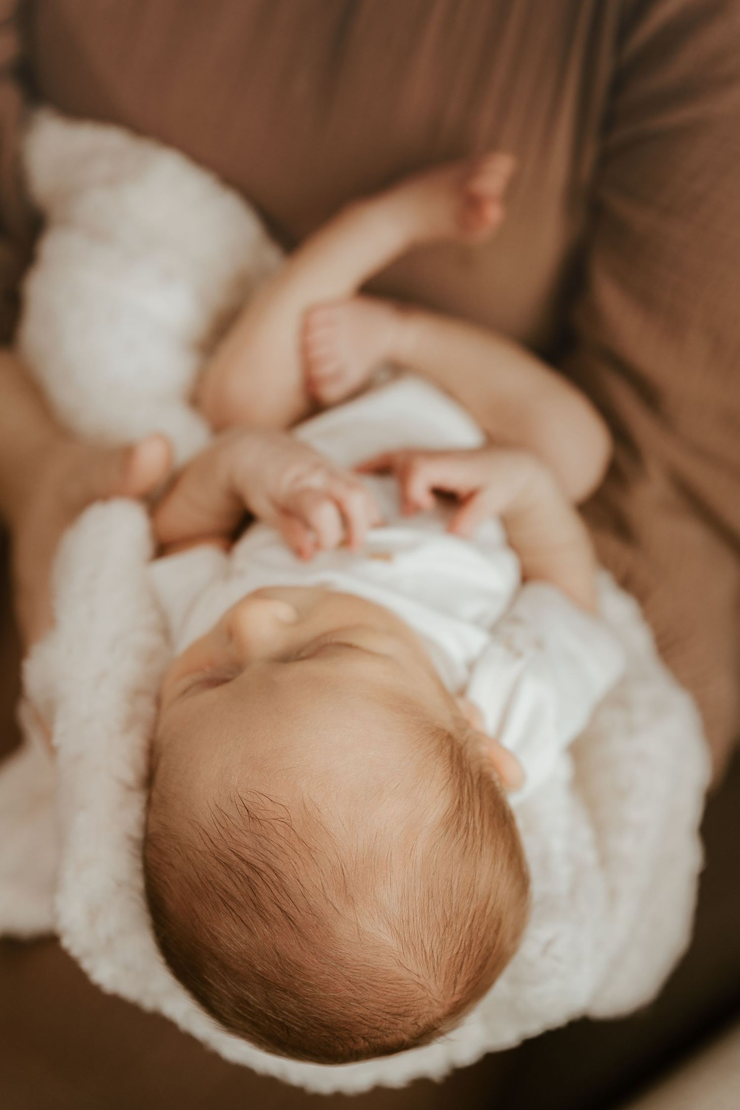 A series of five close-up photos showing a newborn baby wrapped in soft white blankets against a brown background.