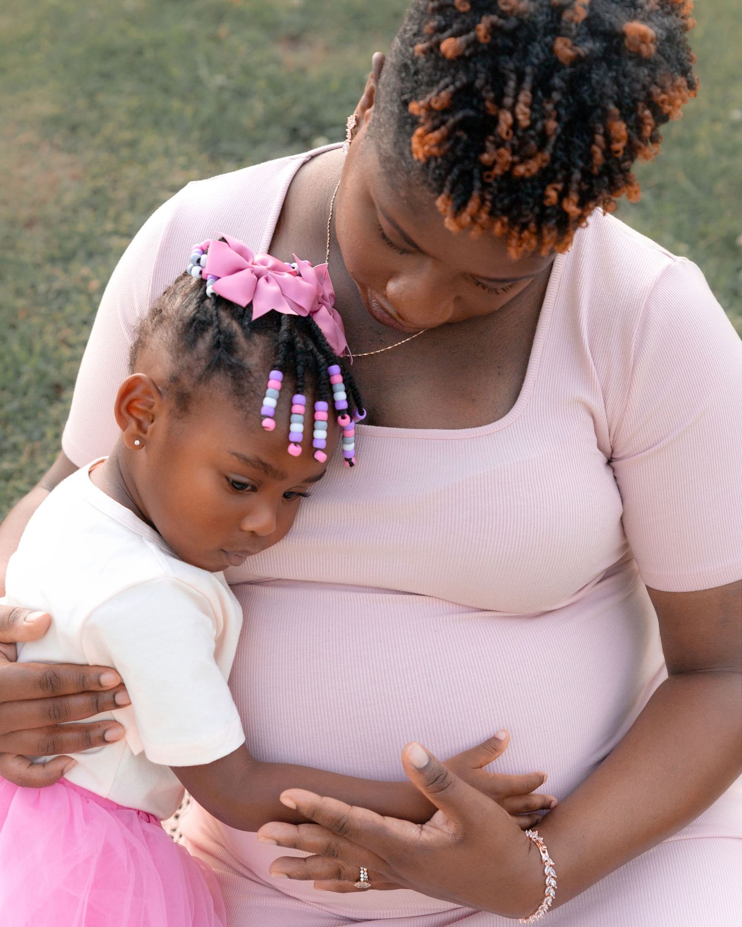 Mother and child share tender moments together in pink outfits during an outdoor maternity photoshoot.