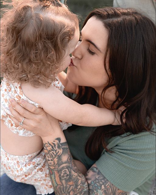 A tender moment shared between a woman in a green shirt with tattoos and a small child in a floral dress.